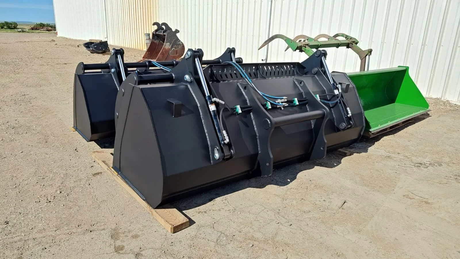 Large black and green industrial attachment for a tractor or skid steer, resting on dirt ground outdoors.