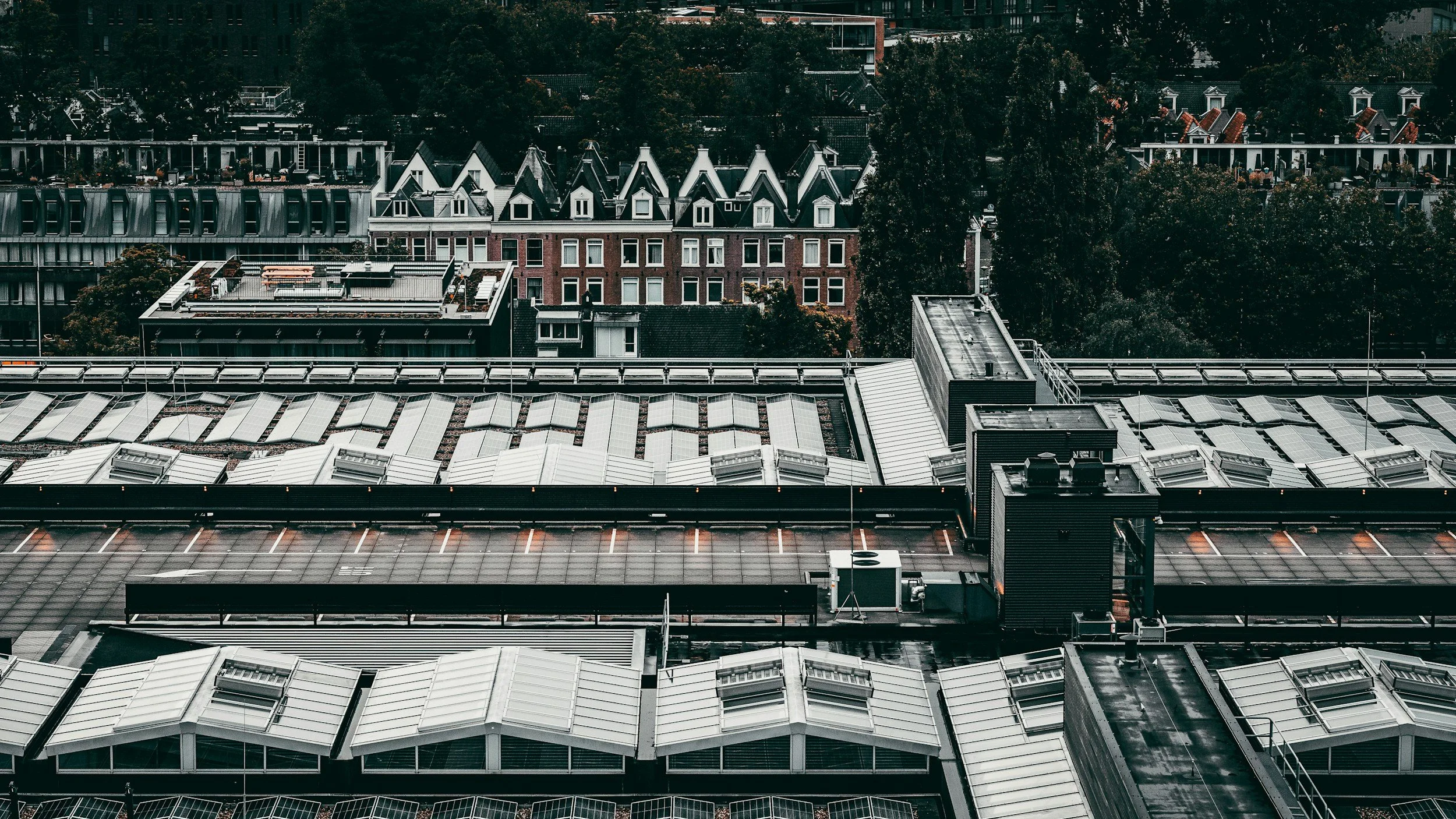 View of a city rooftop with glass-covered skylights and a background of residential buildings with trees.