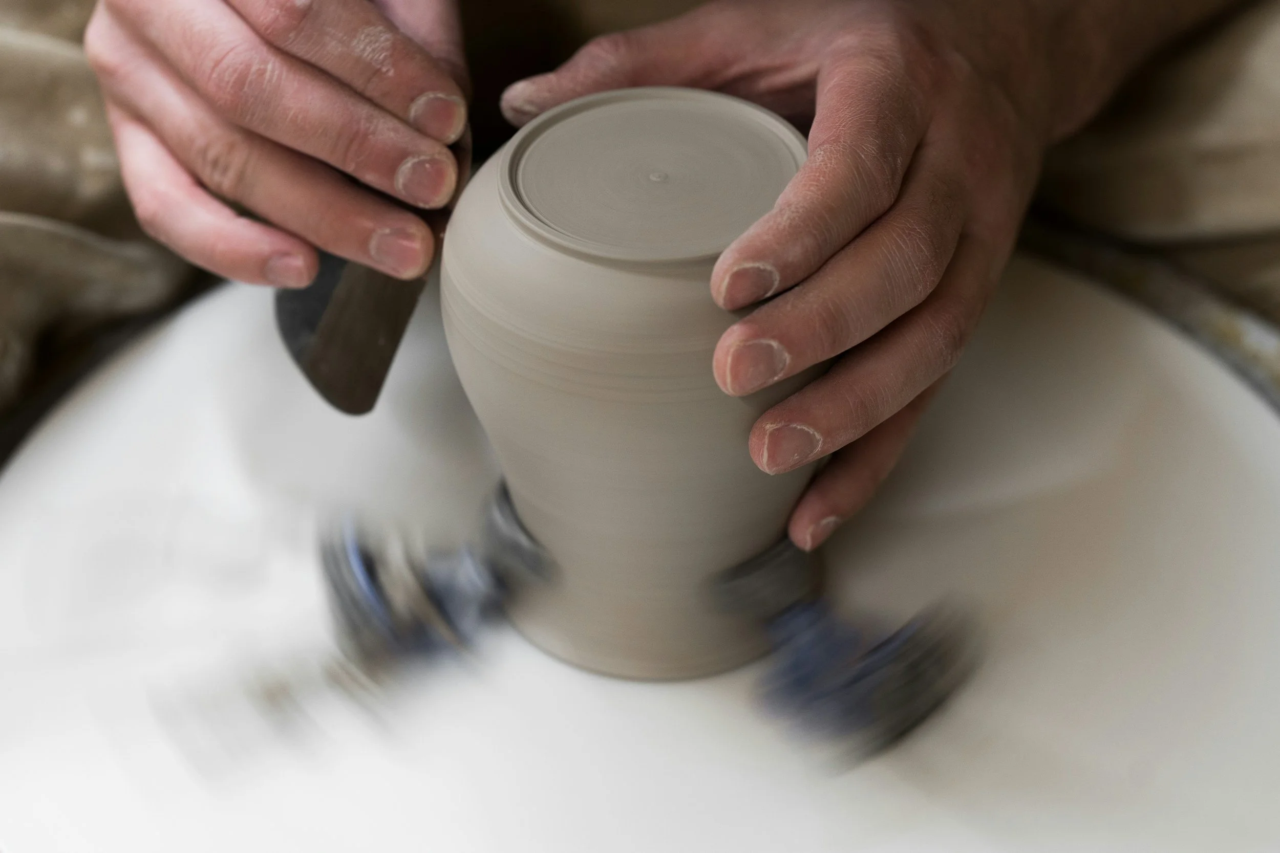 Hands shaping a ceramic pot on a spinning wheel.