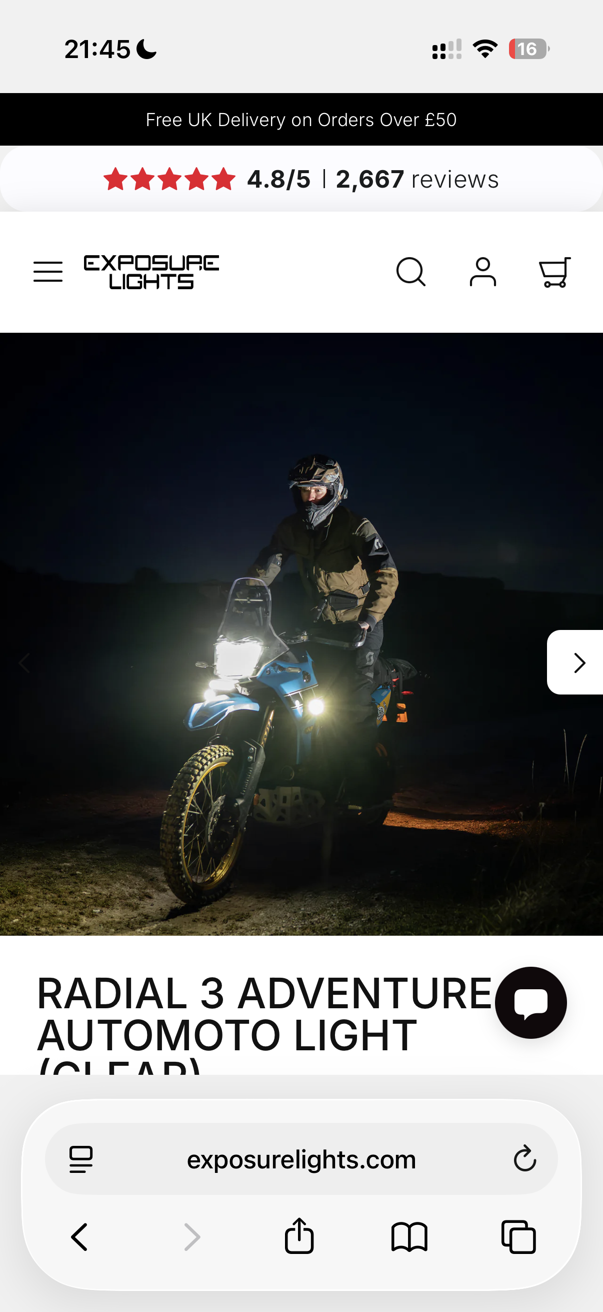 A person wearing a helmet and riding a blue motorcycle at night with headlights on, on a dirt path in a rural area.