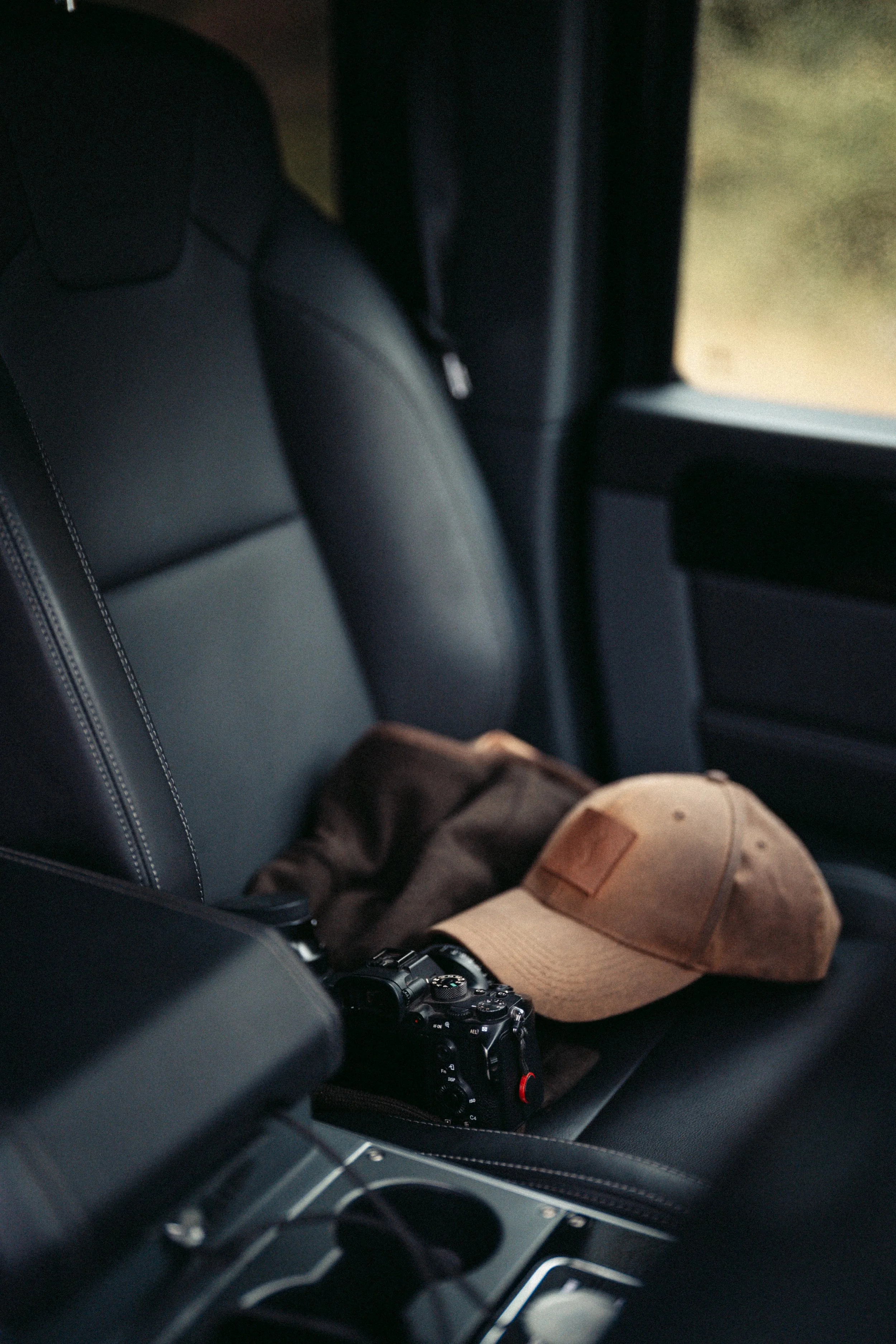The interior of a car showing the backseat with a camera, a tan cap, and brown shoes resting on the seat.