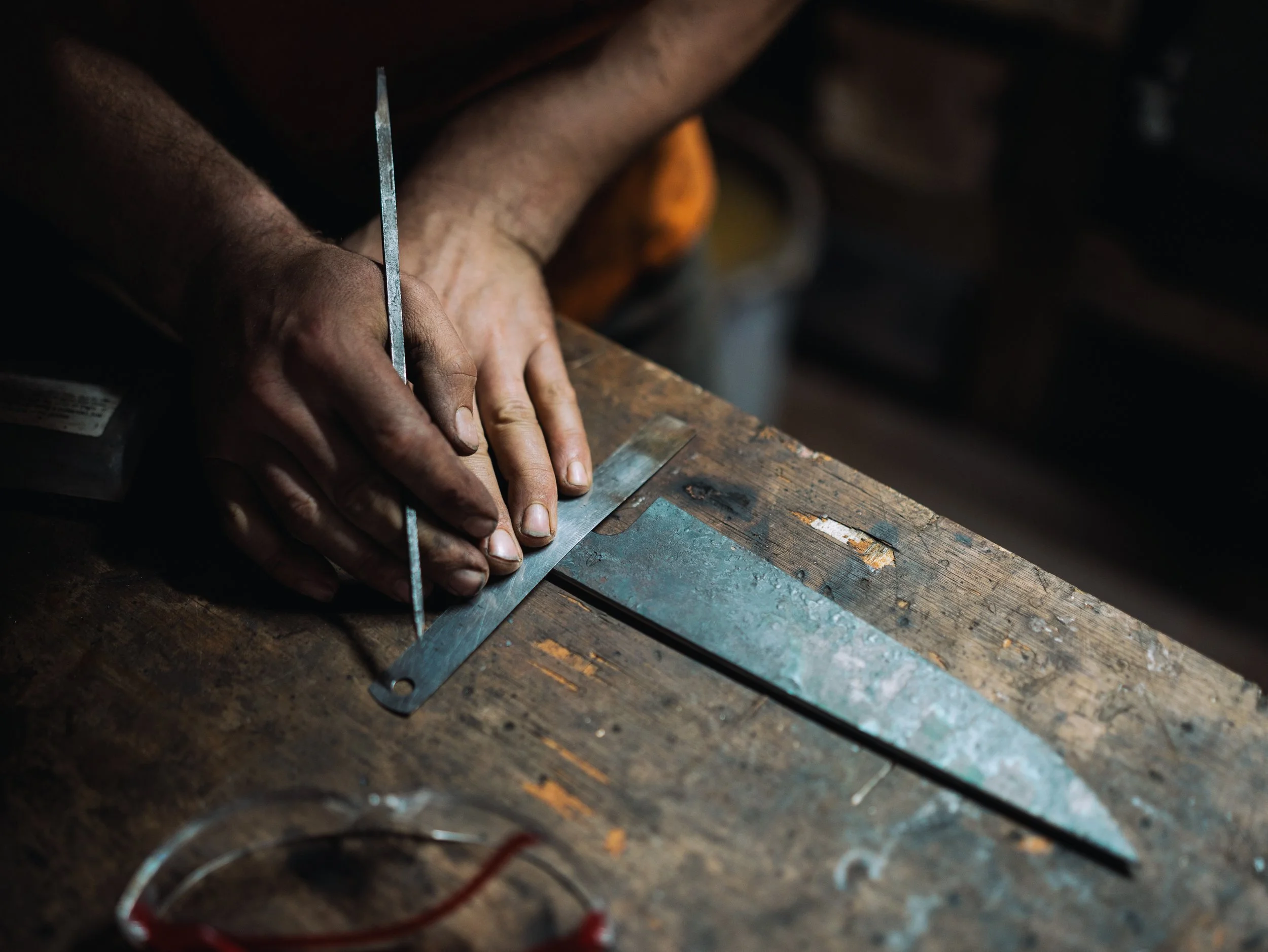 Close-up image of a person using a fine metal file to shape a piece of metal on a workbench in a workshop