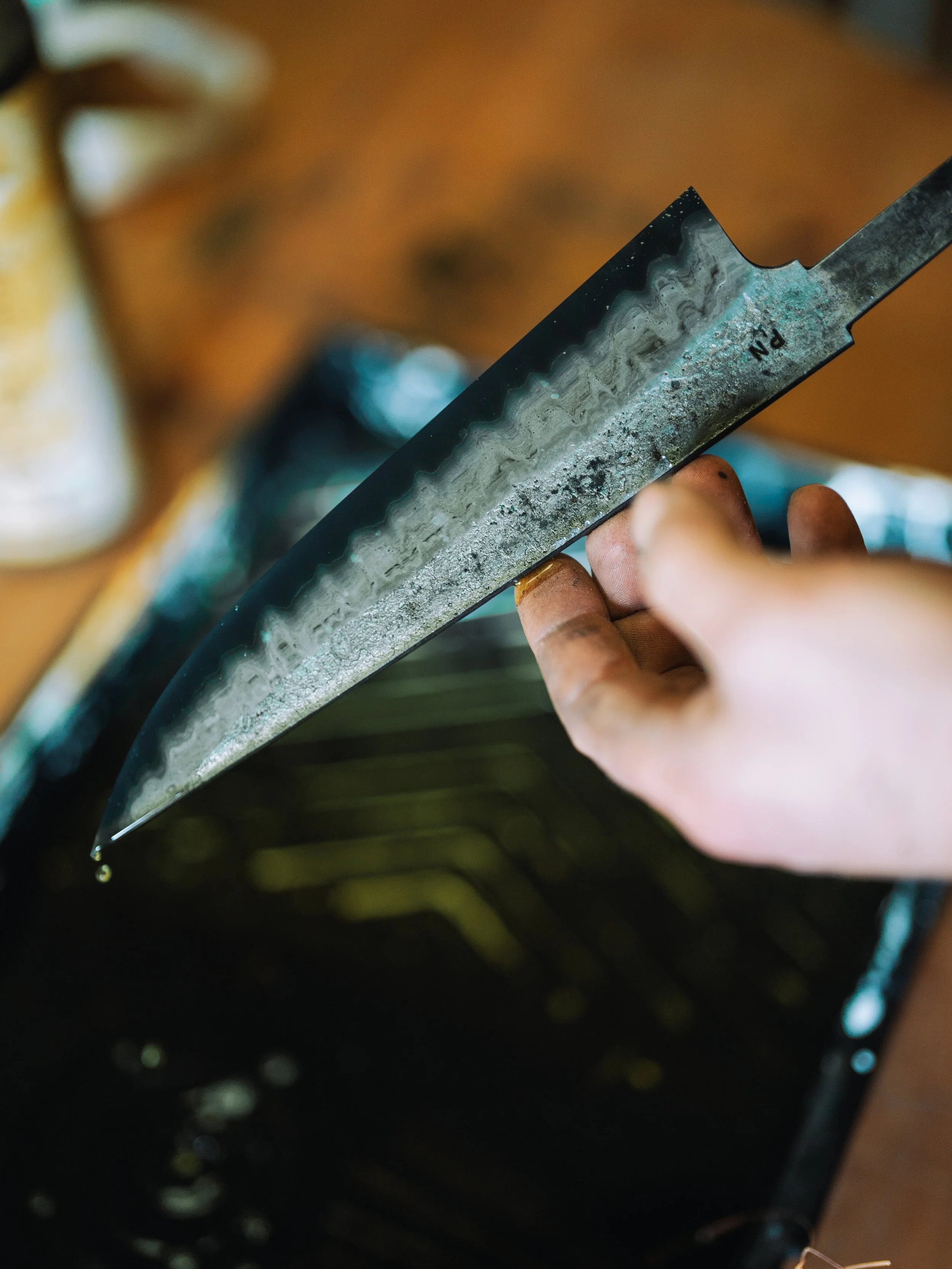 A person holding a rusty straight razor with a tarnished blade, with a blurred background of tools and objects.