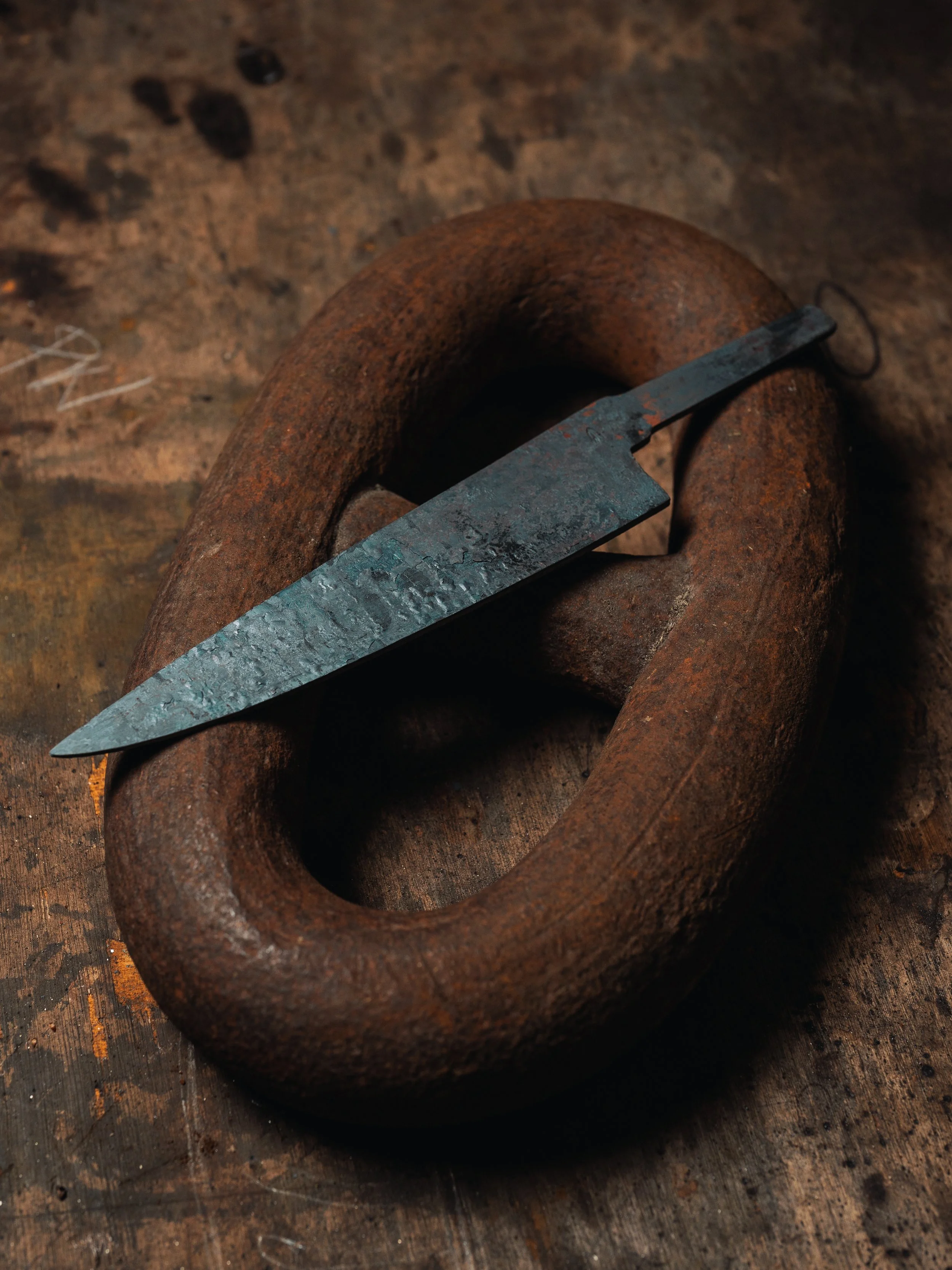 Close-up of a rusty metal shackle with a metal tool resting on it, on a rough wooden surface.