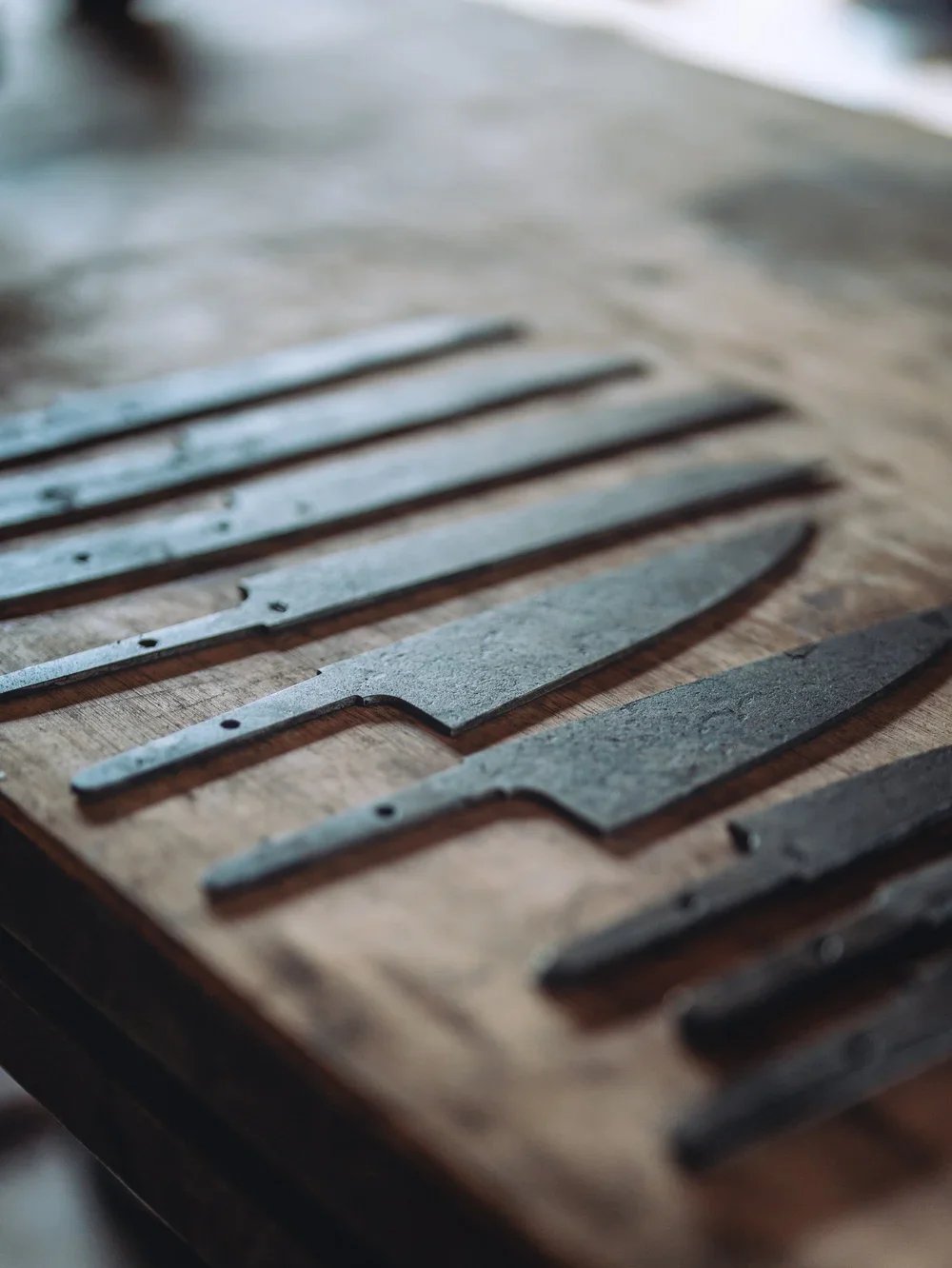 Close-up of blacksmithing knives or tools on a wooden surface.