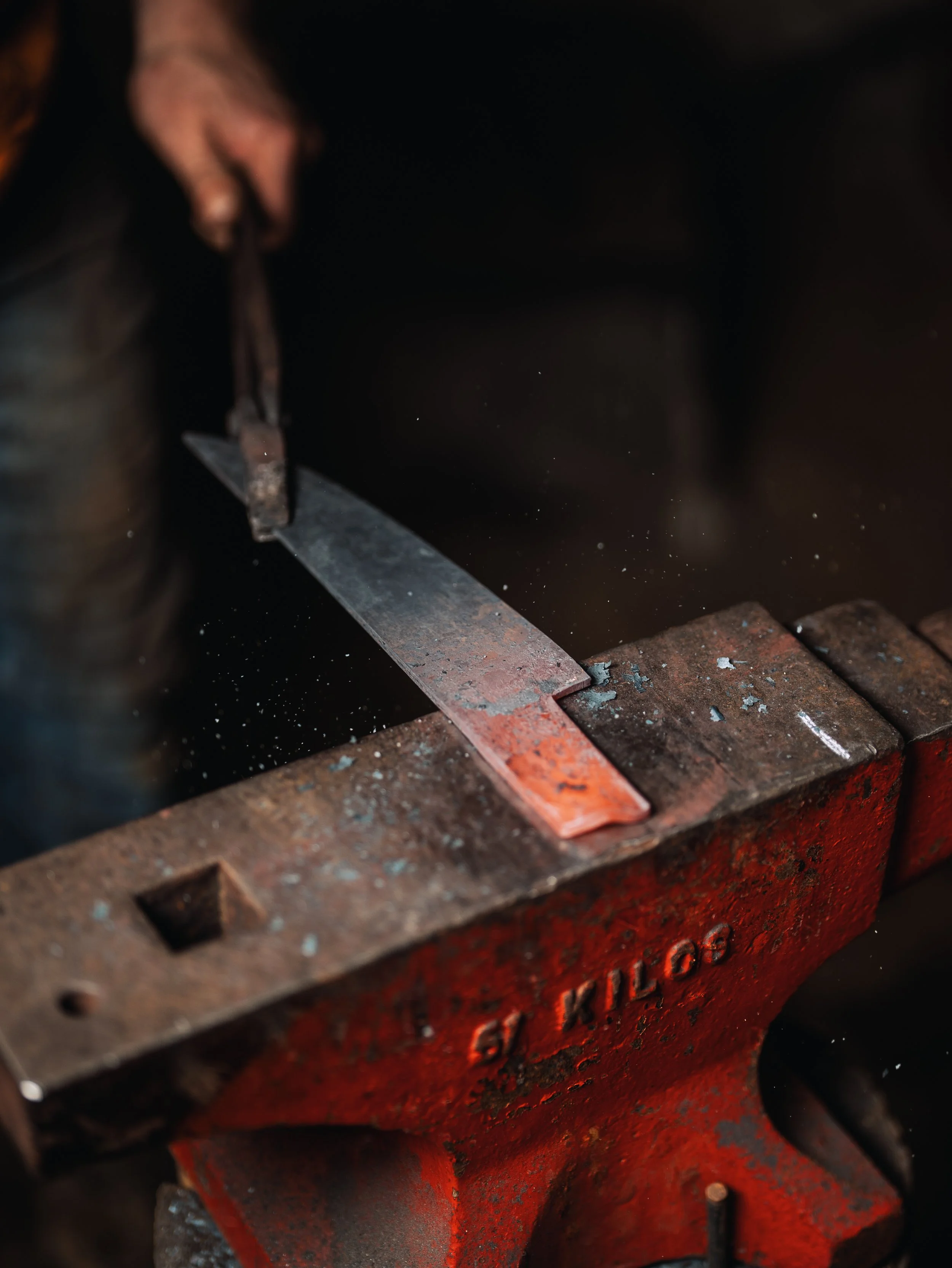 A hand holding tongs grasping hot metal in a forge with glowing red surface.