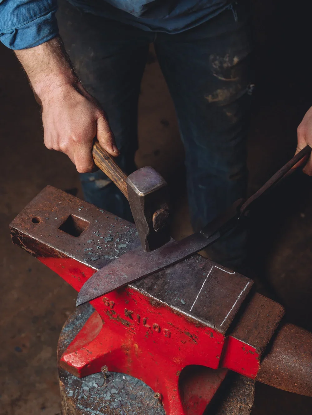 A person is using a hammer and an anvil to shape a piece of metal in a blacksmith shop.