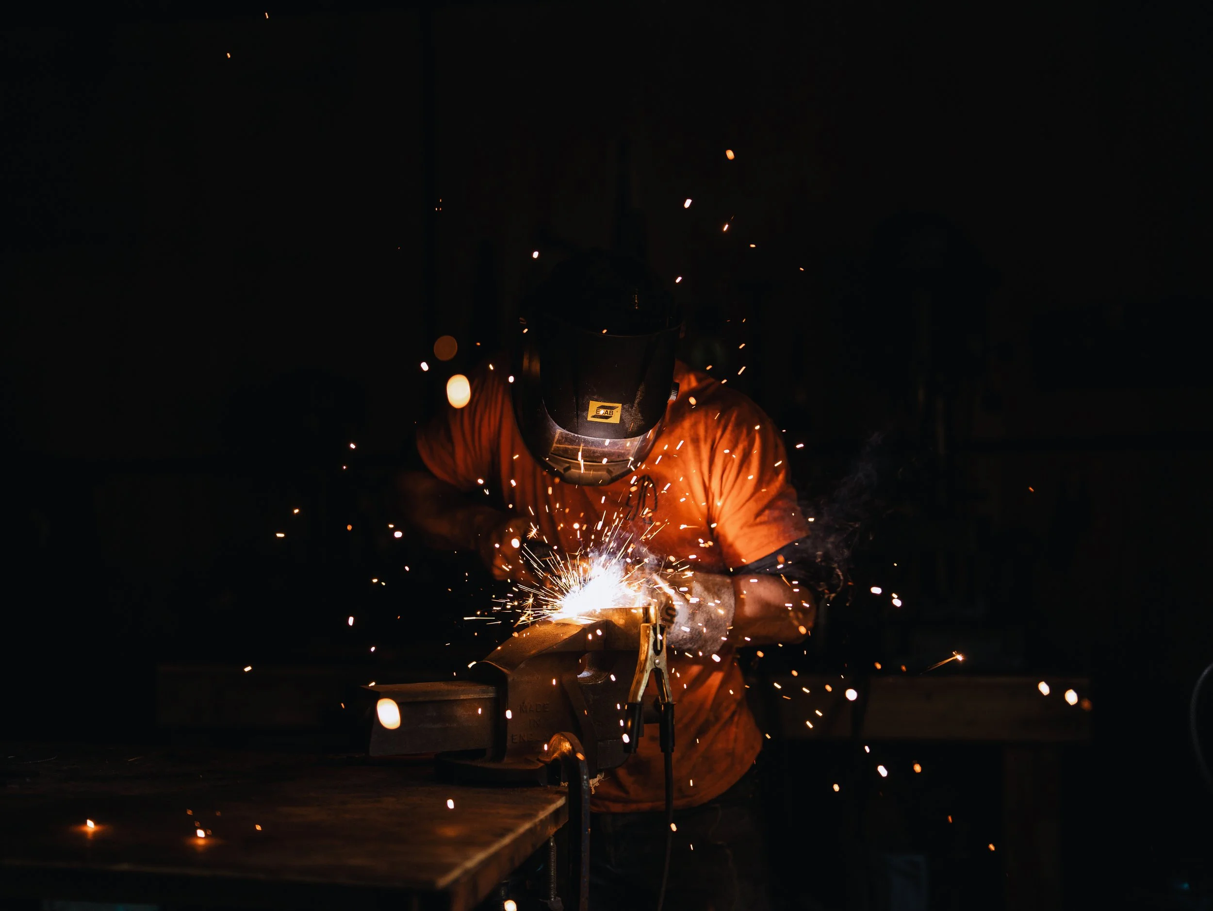 A welder wearing protective gear welding metal, with sparks flying around in a dark environment.