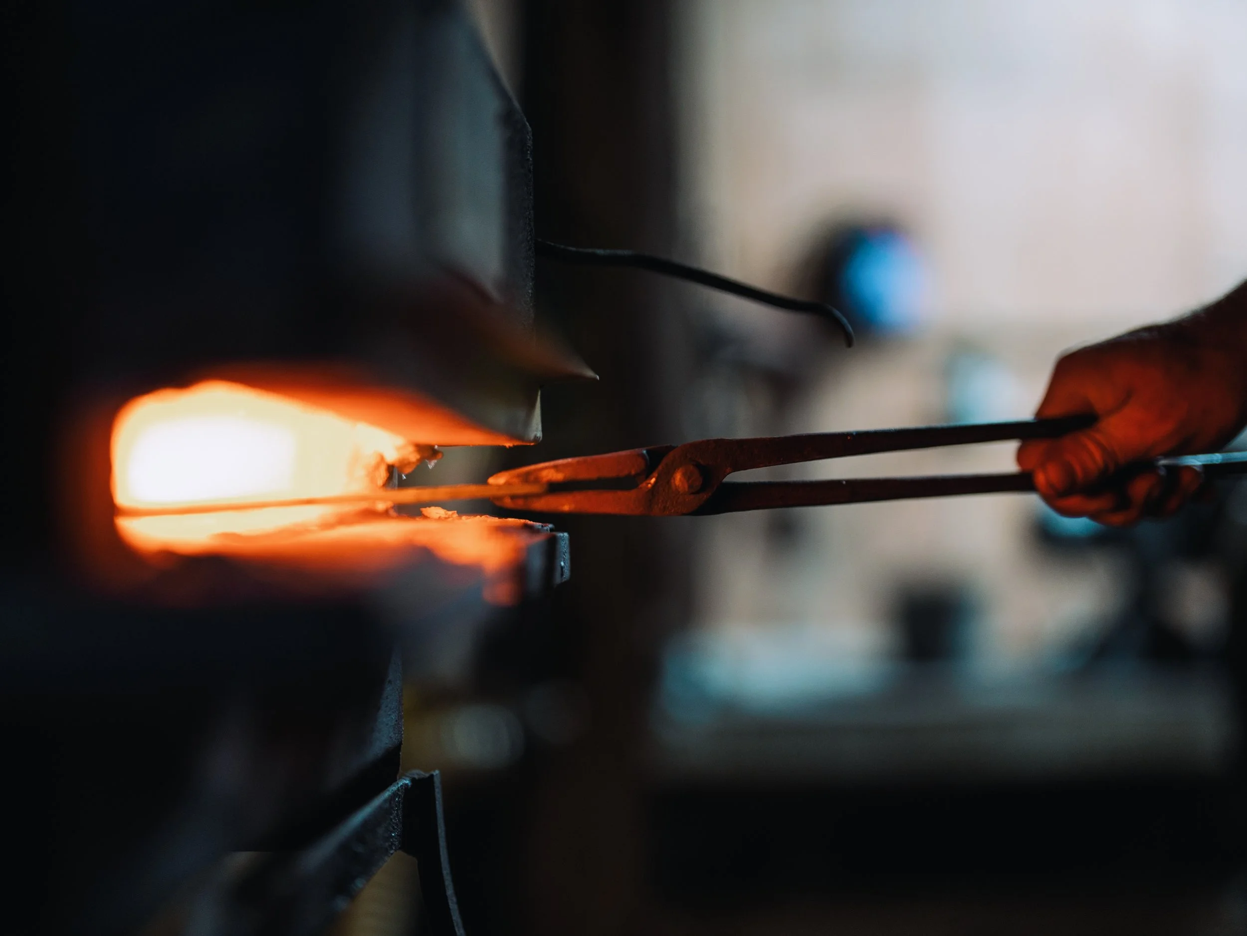 Close-up of a glowing hot piece of metal being handled with tongs in a blacksmithing or metalworking setting.