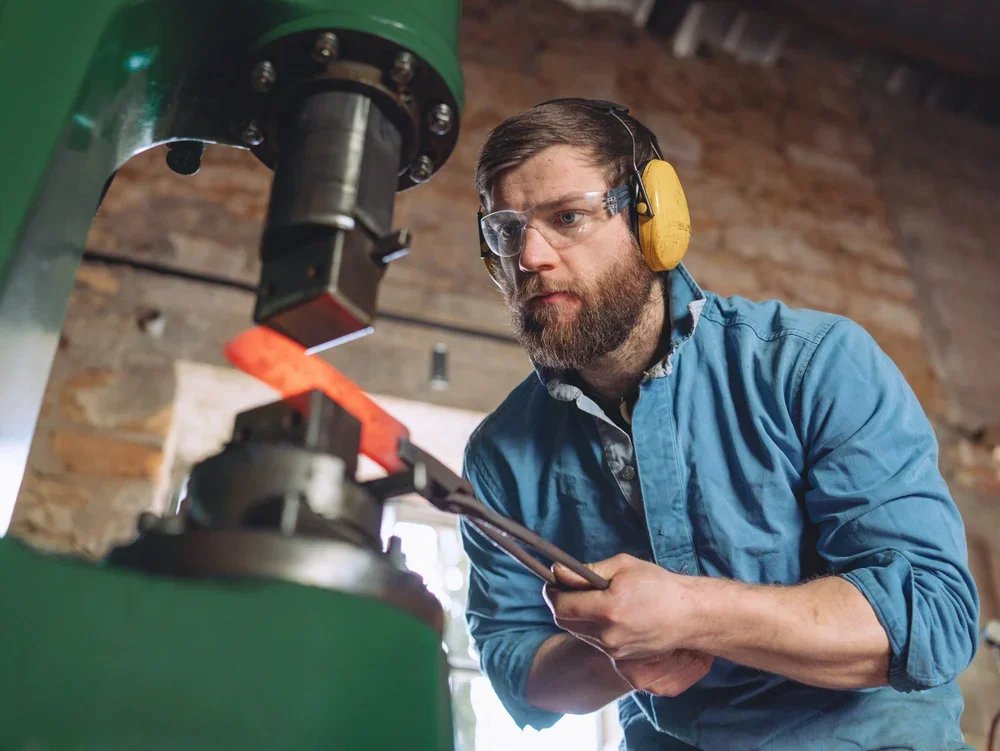A man wearing safety glasses and ear protection operating a hydraulic press in a workshop.