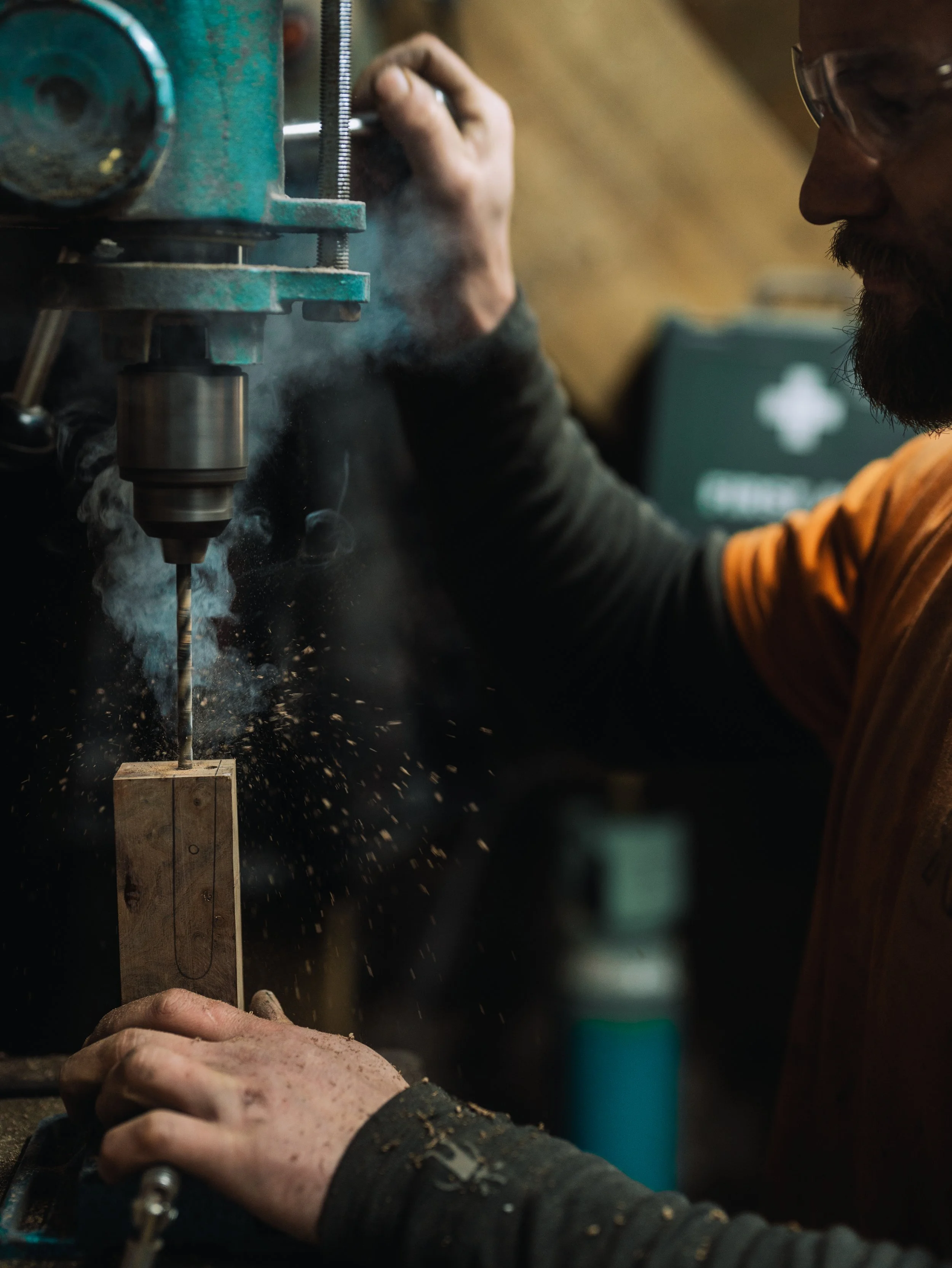 A person using a drill press to drill into a piece of wood, with sparks flying from the drilling process.