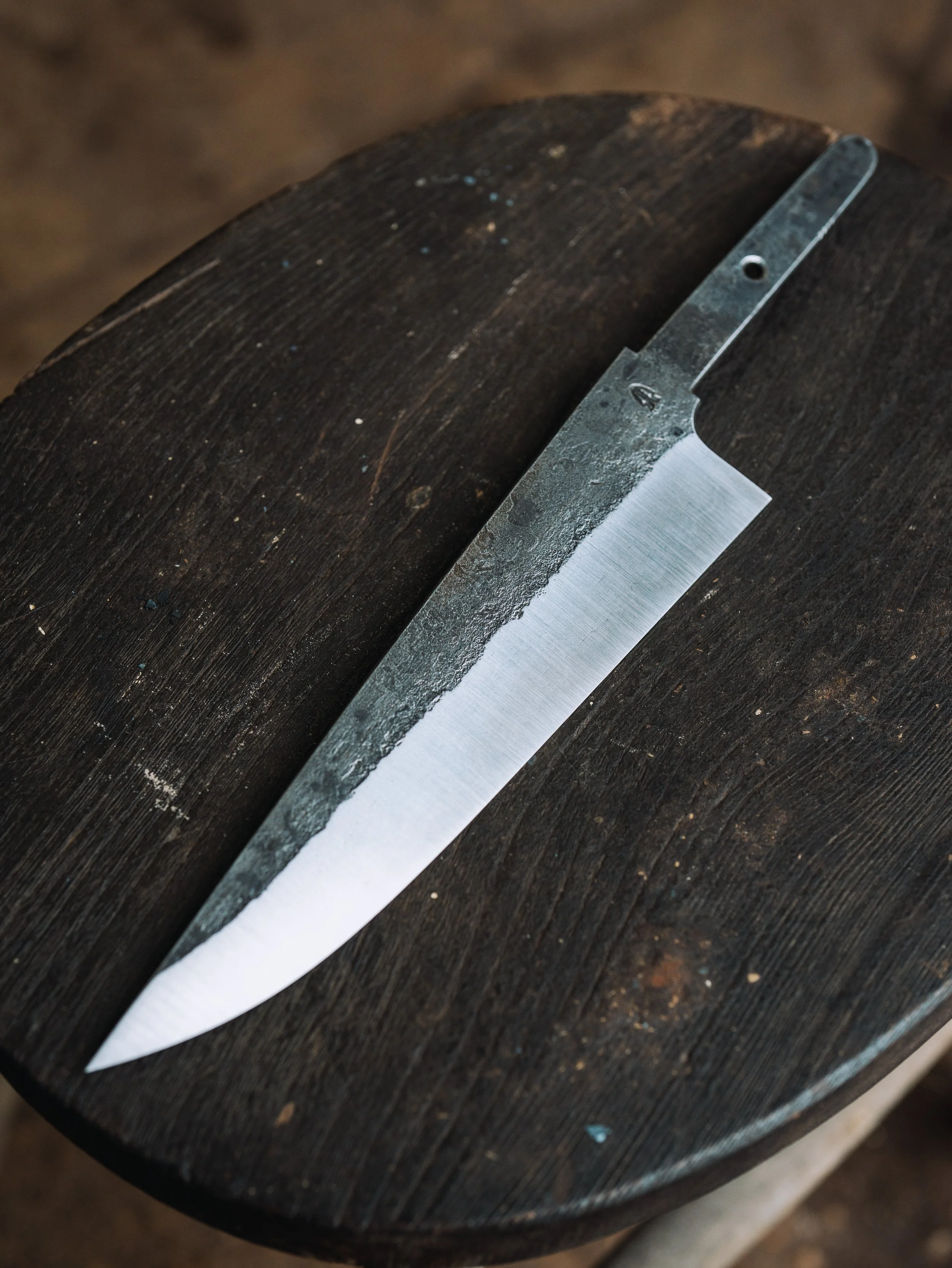 A metal straight razor with a partially textured handle resting on a dark wooden surface.
