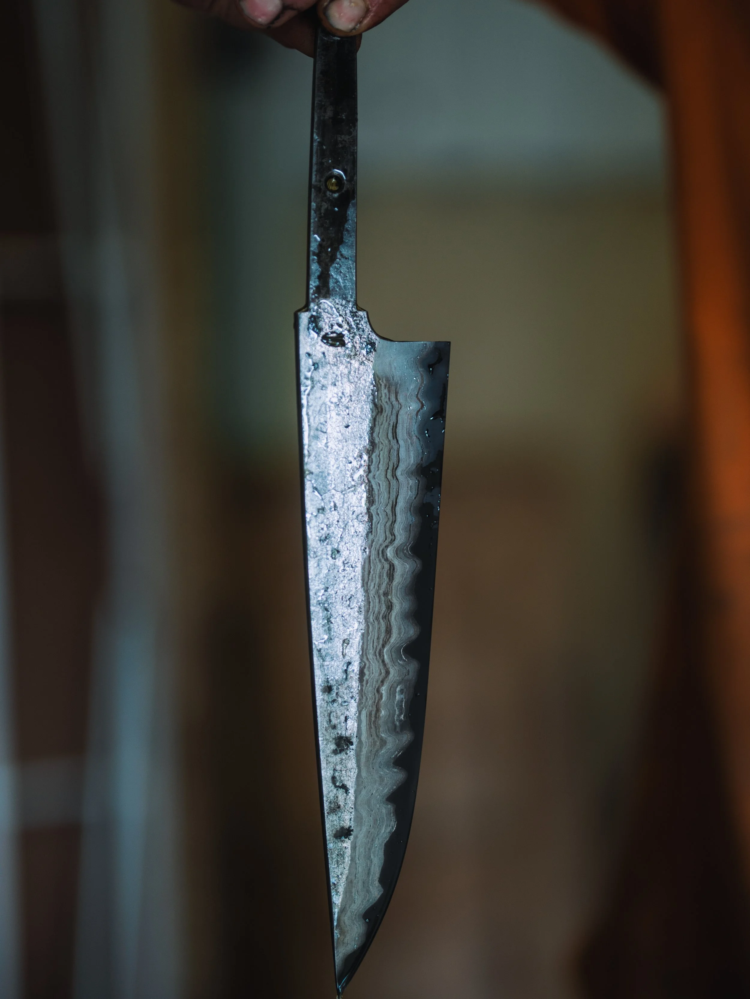 Close-up of a metal knife with a textured blade, held by fingers with dirt under the nails.