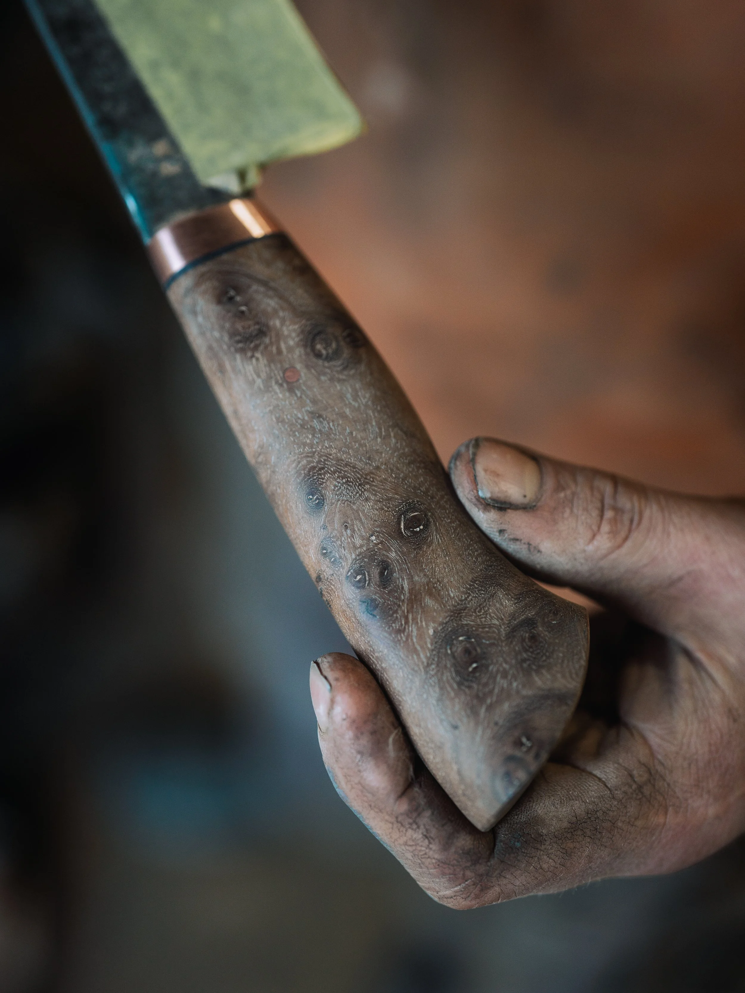 Close-up of a person’s hand holding a wood carving chisel with a wooden handle and a metal blade.