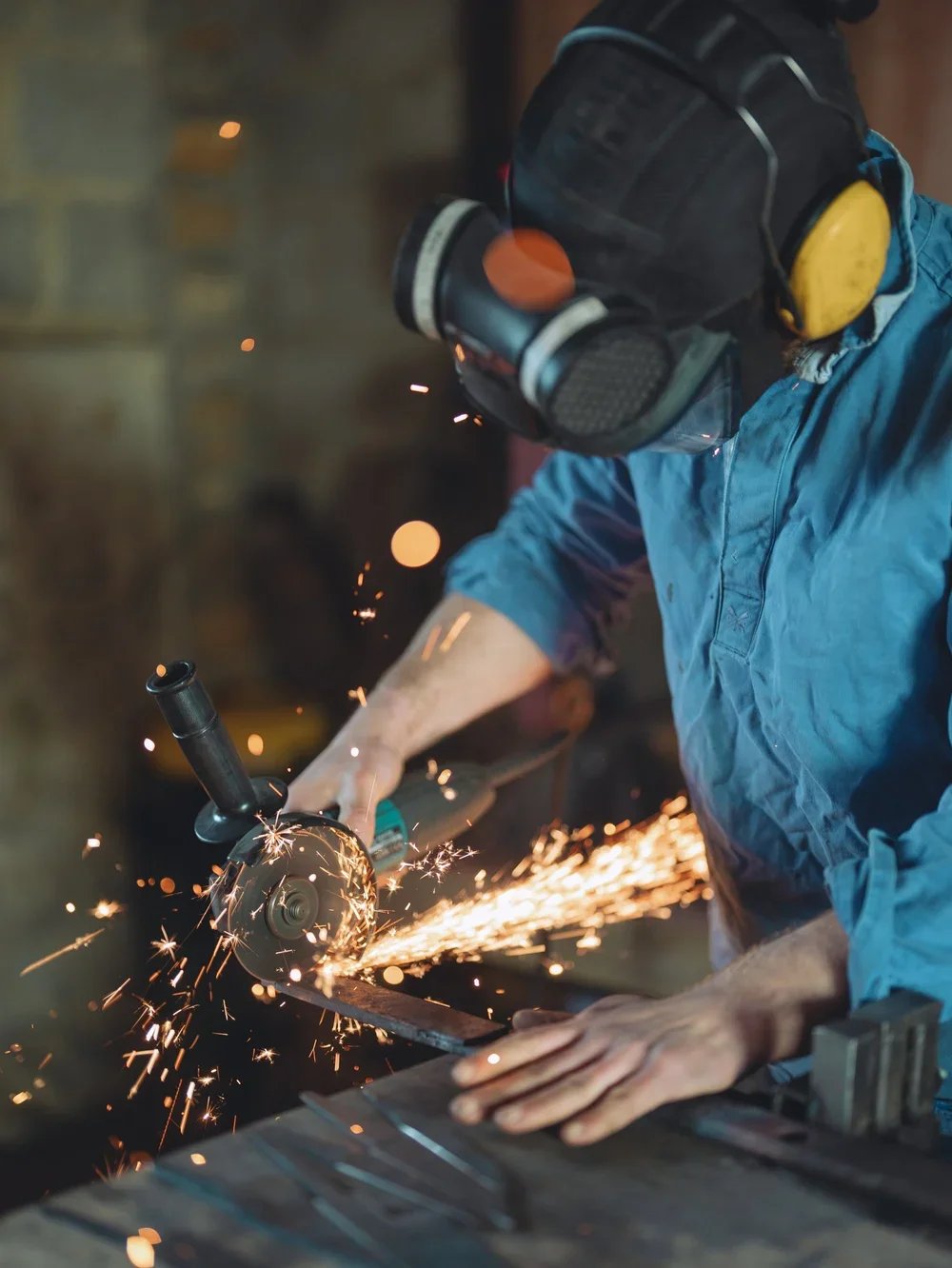 A worker cutting metal with an angle grinder, sparks flying, wearing a helmet and protective gear.