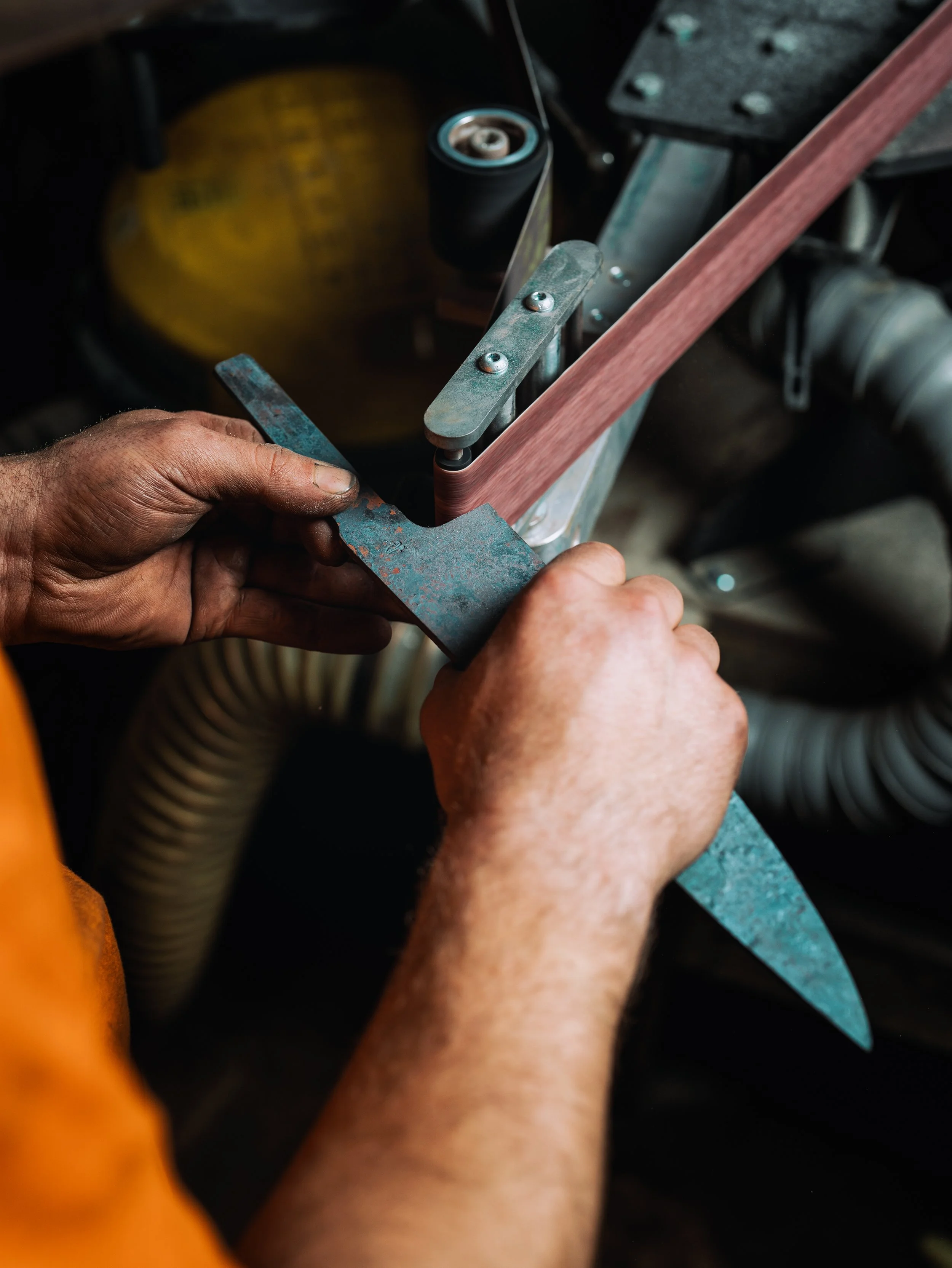 Close-up of a person's hands sanding a piece of wood, with tools and equipment around.