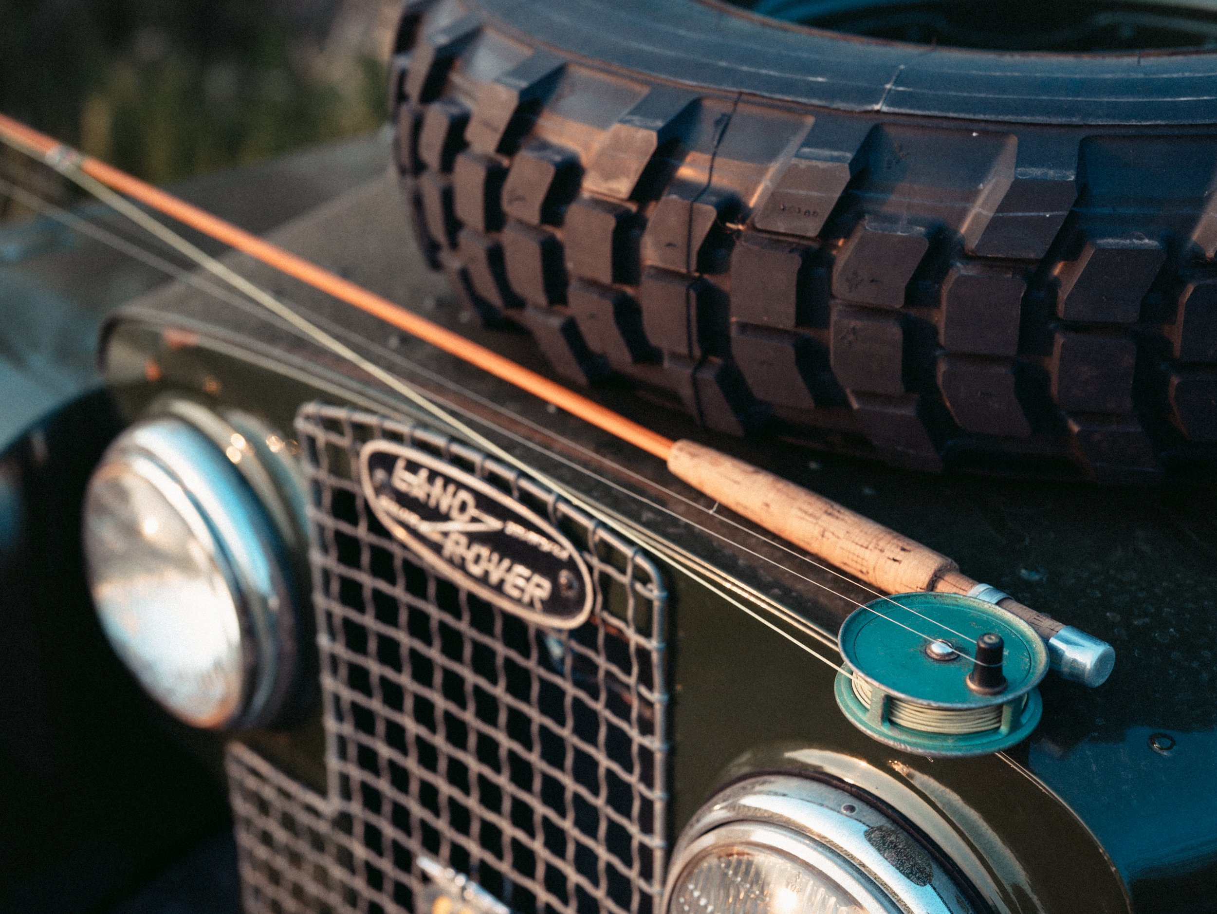 Close-up of a vintage Triumph TR-7 car's front grille, headlight, and chrome bumper with a focus on the black grid grille and round headlight.