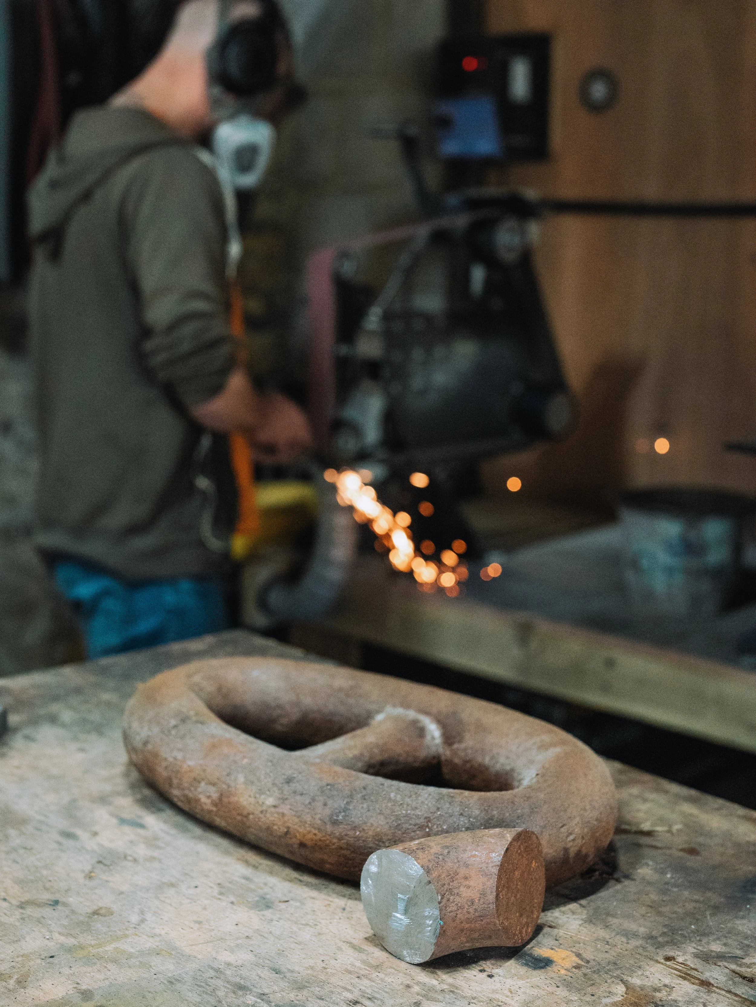 Cloth with cloth and glass, which looks like a part of a desk. In the background, a person is working with a computer and welding equipment, with sparks flying.