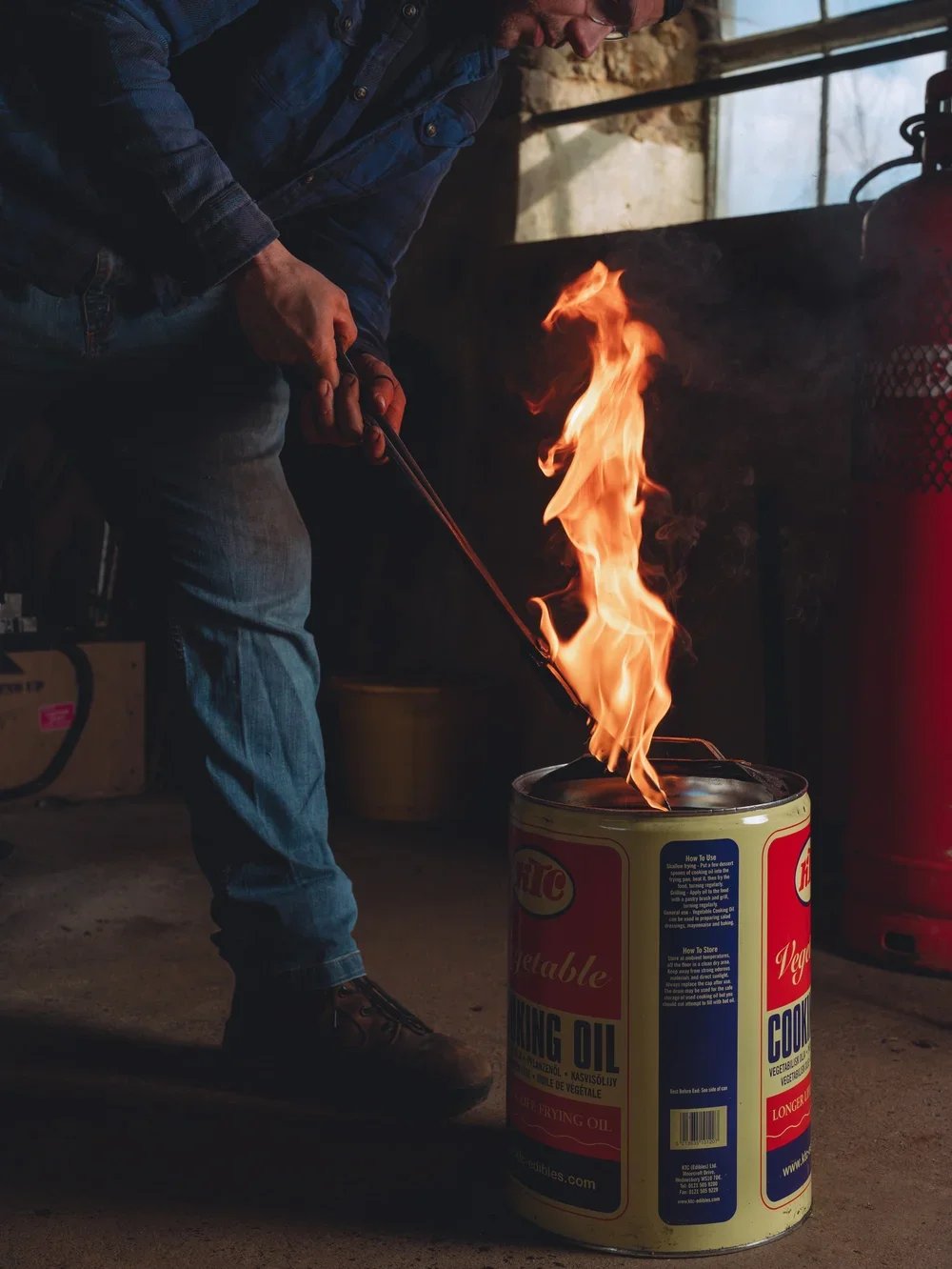 Man igniting a flame in a can of cooking or frying oil in a workshop or garage setting.