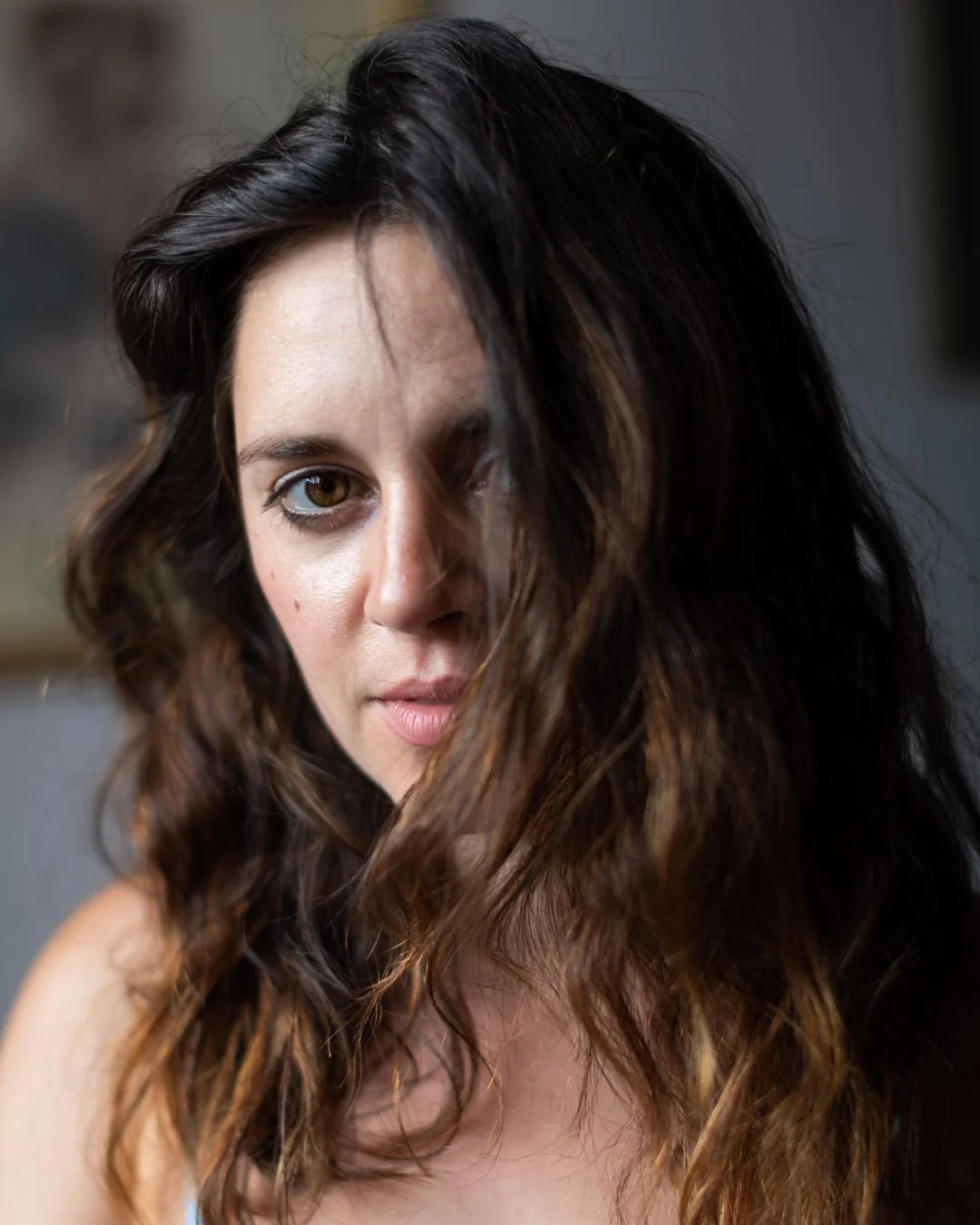 A woman with wavy brown hair and light skin looking into the camera, partially obscured by her hair.