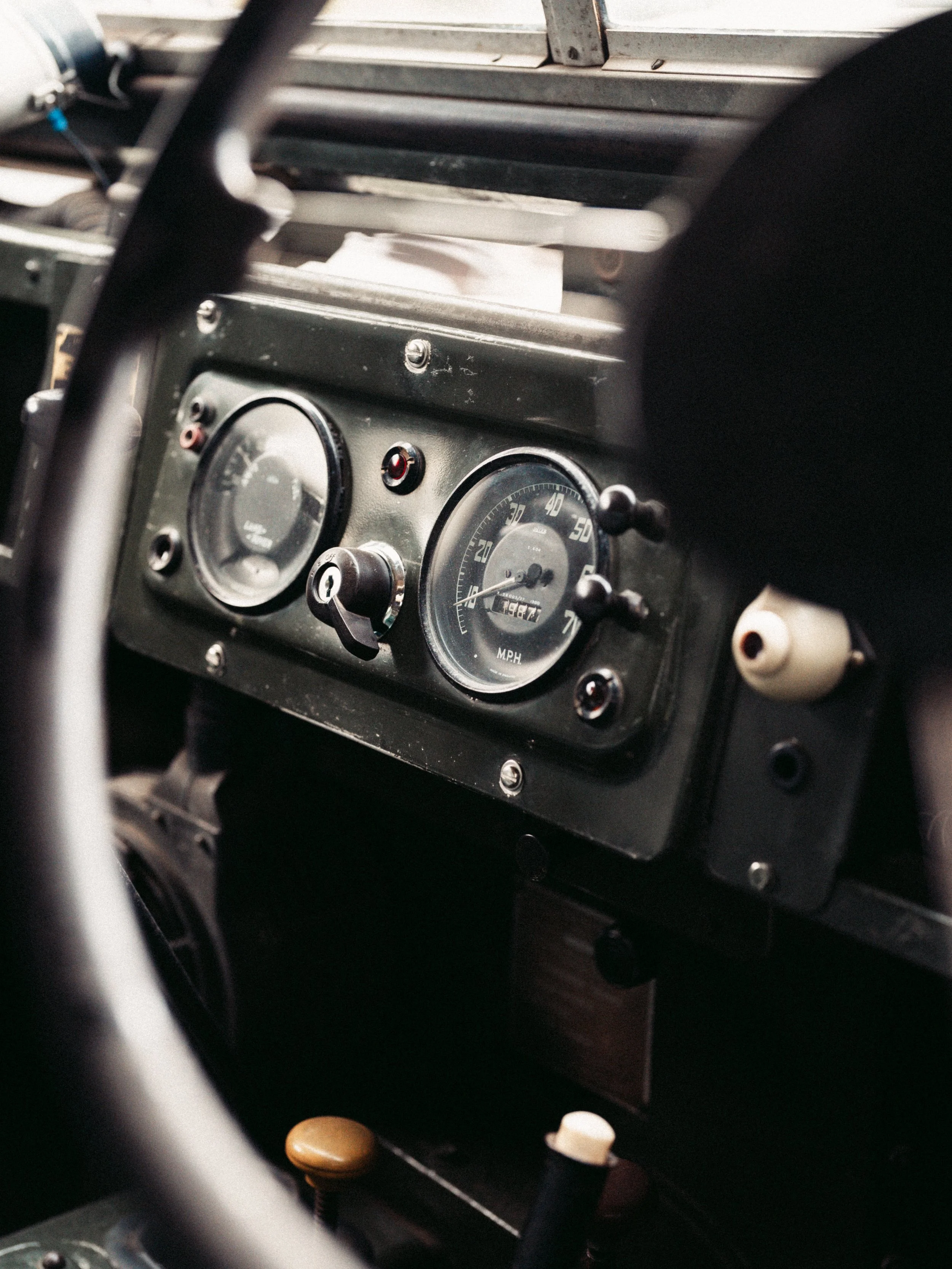 Close-up view of an old car dashboard with analog gauges showing speed and other metrics, partially obscured by a steering wheel.
