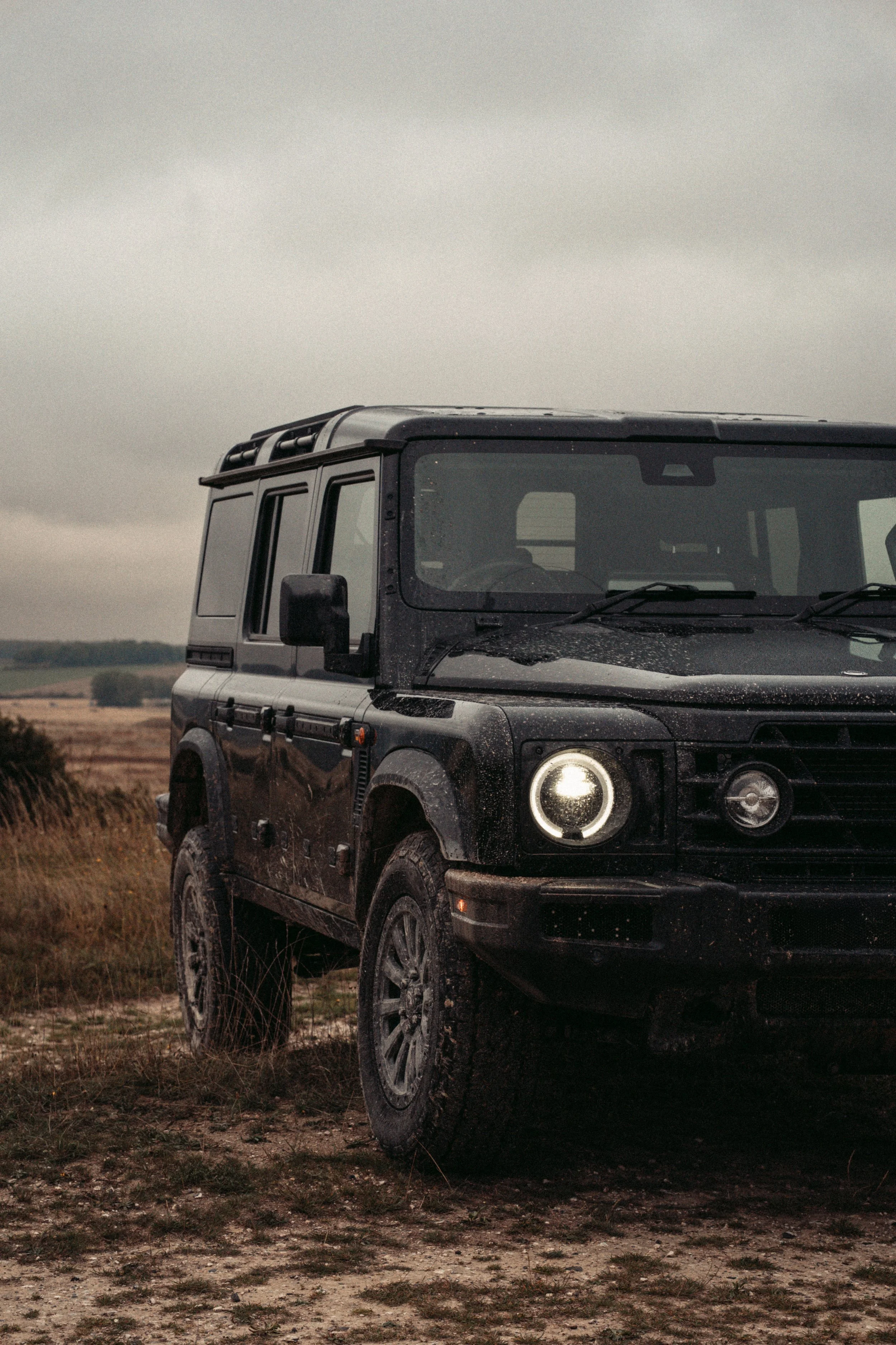 A black off-road SUV parked on a dirt and grassy field under a cloudy overcast sky.