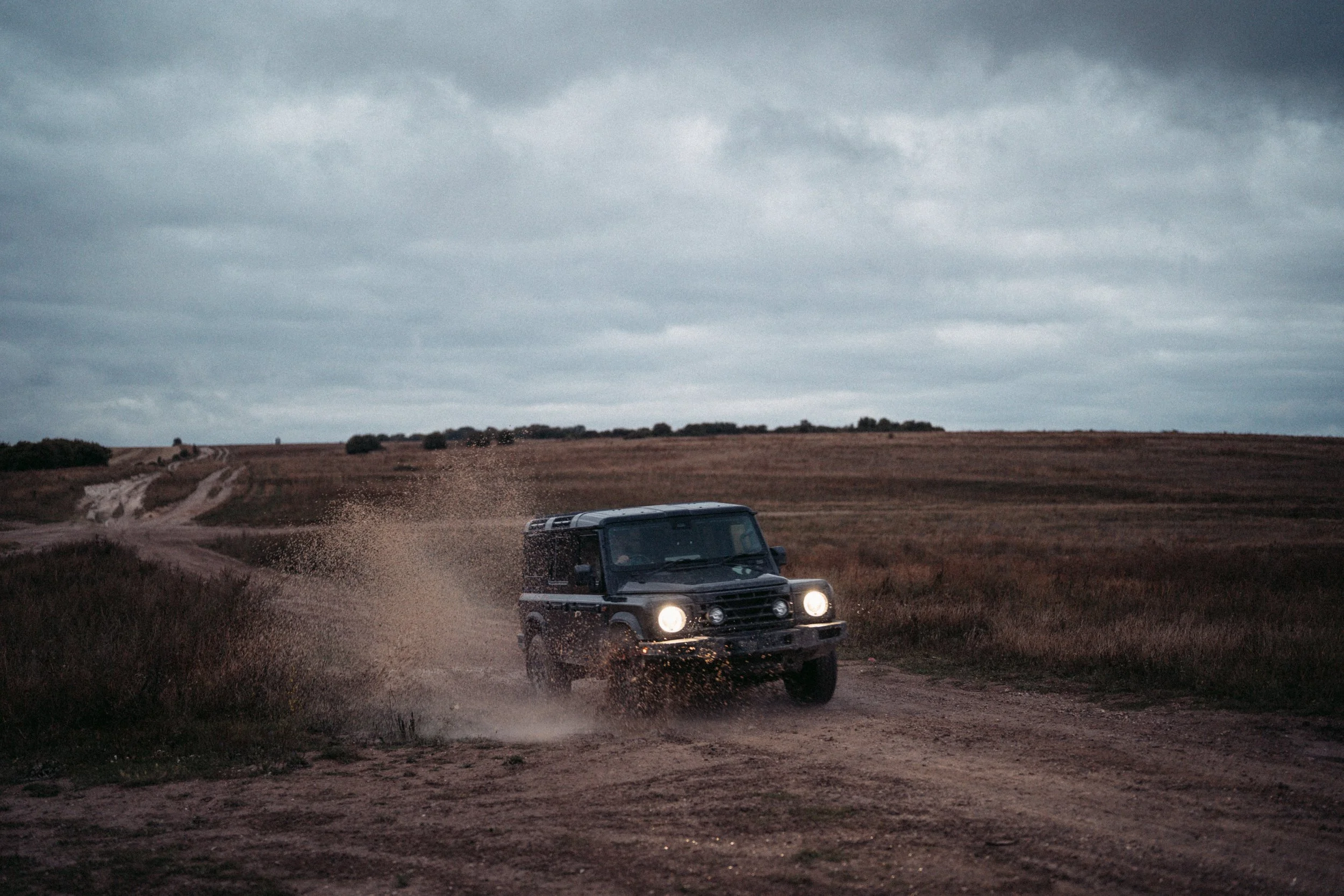 A black off-road vehicle driving on a dirt path in a rural landscape with overcast skies.