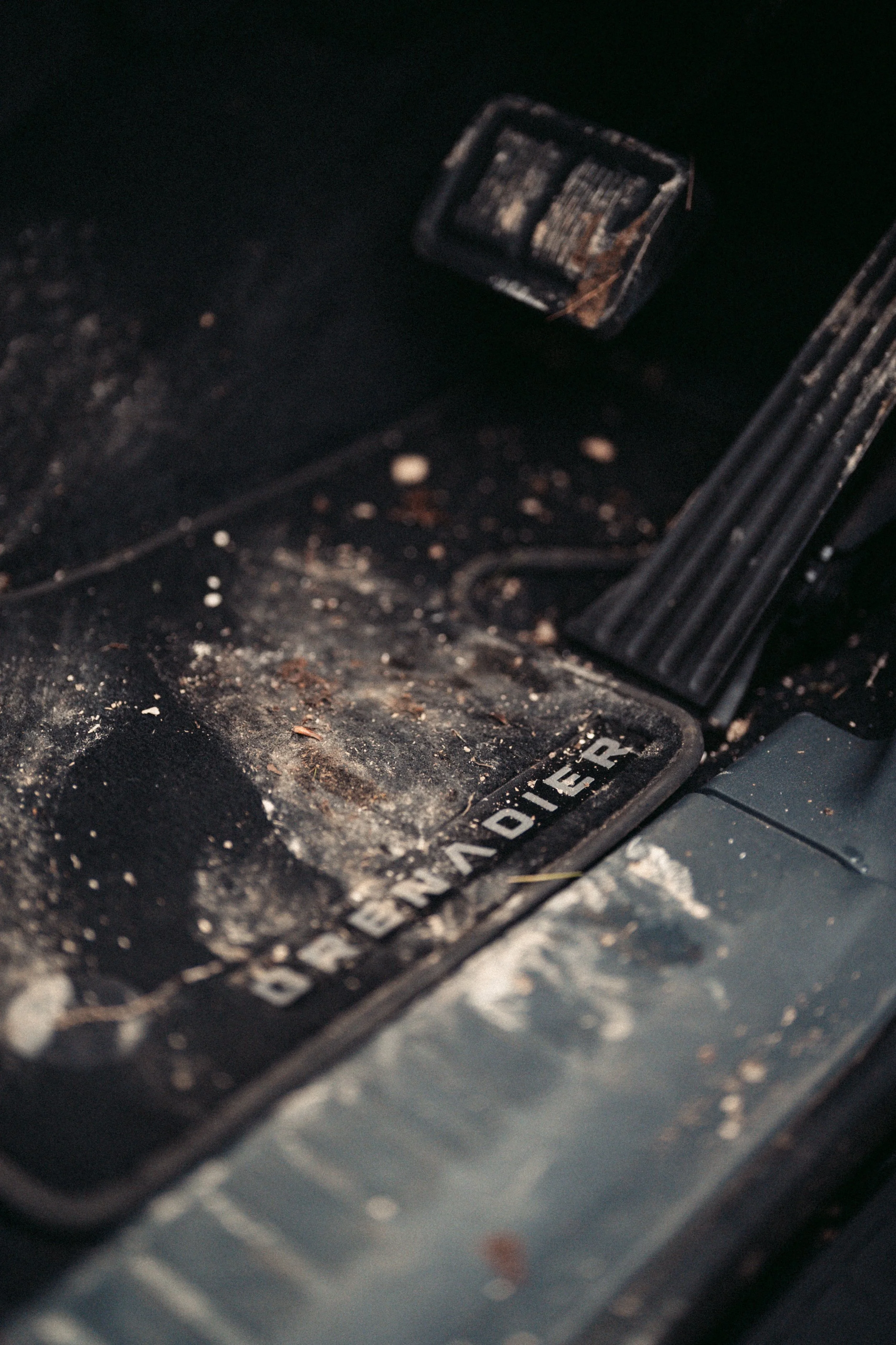 Close-up of a dirty, dusty car interior pedal and floor mat, with a partially visible faded logo.