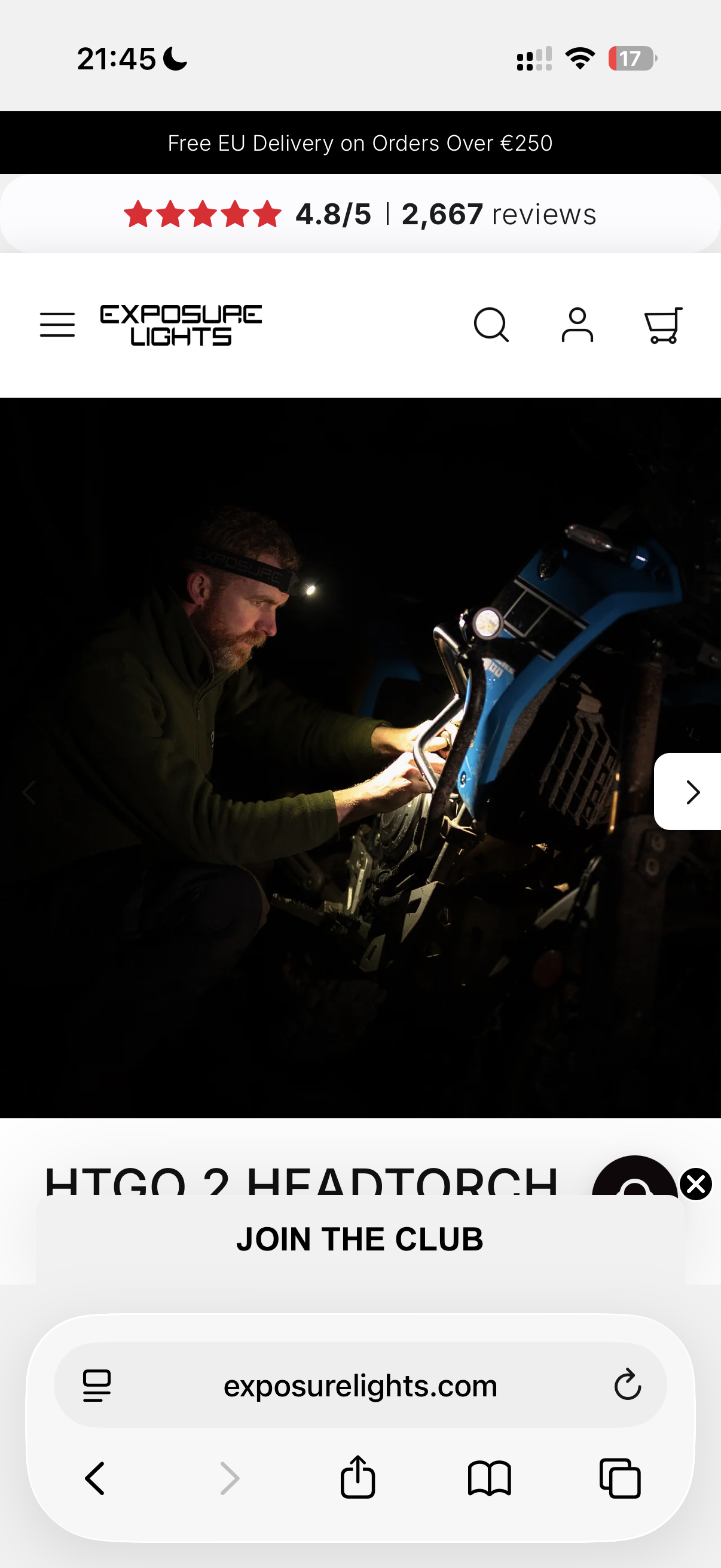 A man wearing a headlamp and black jacket working on a blue off-road vehicle in a dark environment, illuminated by the headlamp.