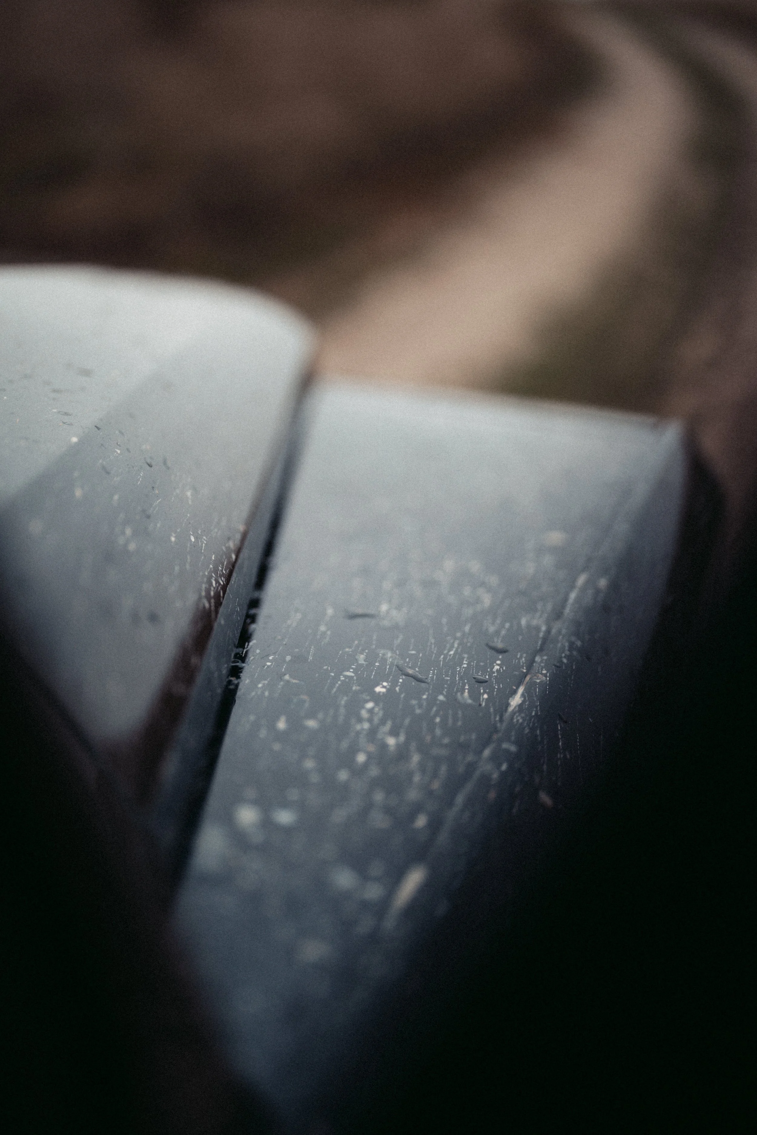 Close-up of a metallic surface with water droplets, showing a slightly curved edge and a dark background.