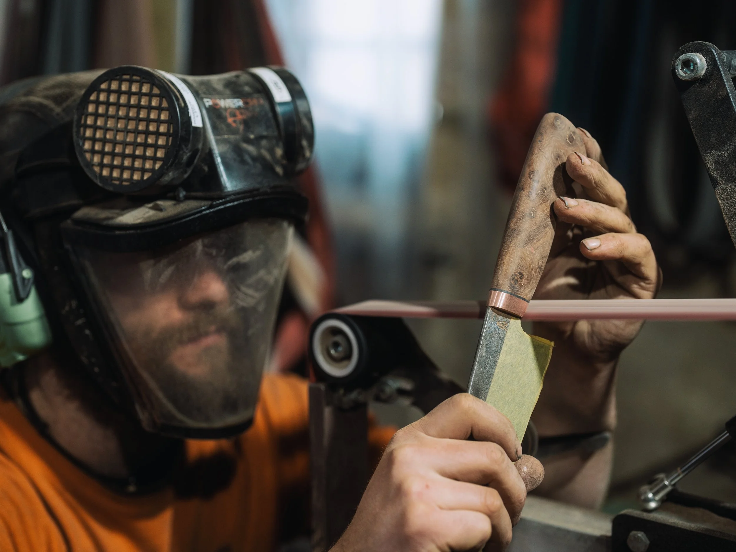 Close-up of a person building or repairing something, holding a small tool with both hands. Items like goggles and a screwdriver are visible.