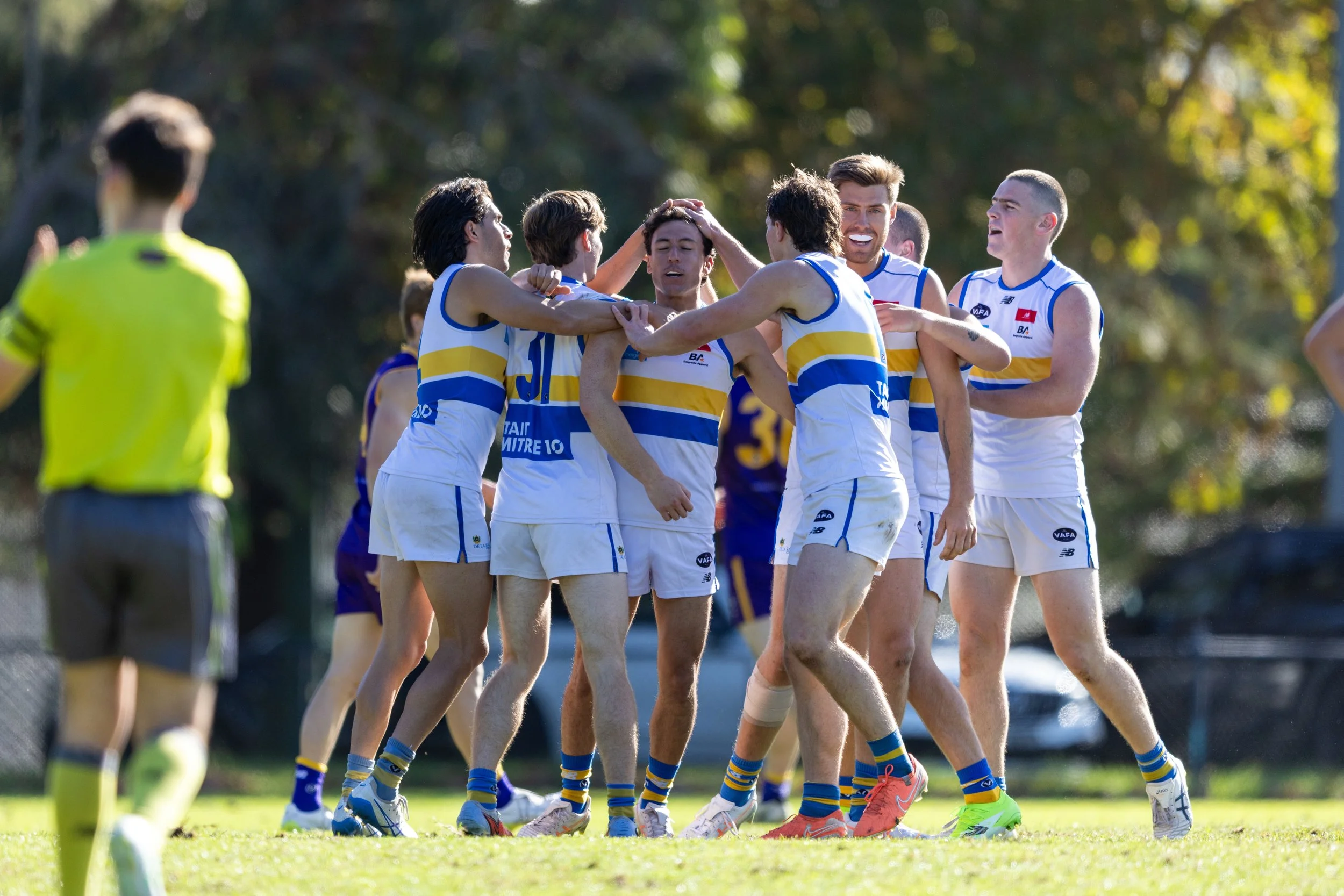 Group of athletes celebrating on a sports field with a referee in the foreground.