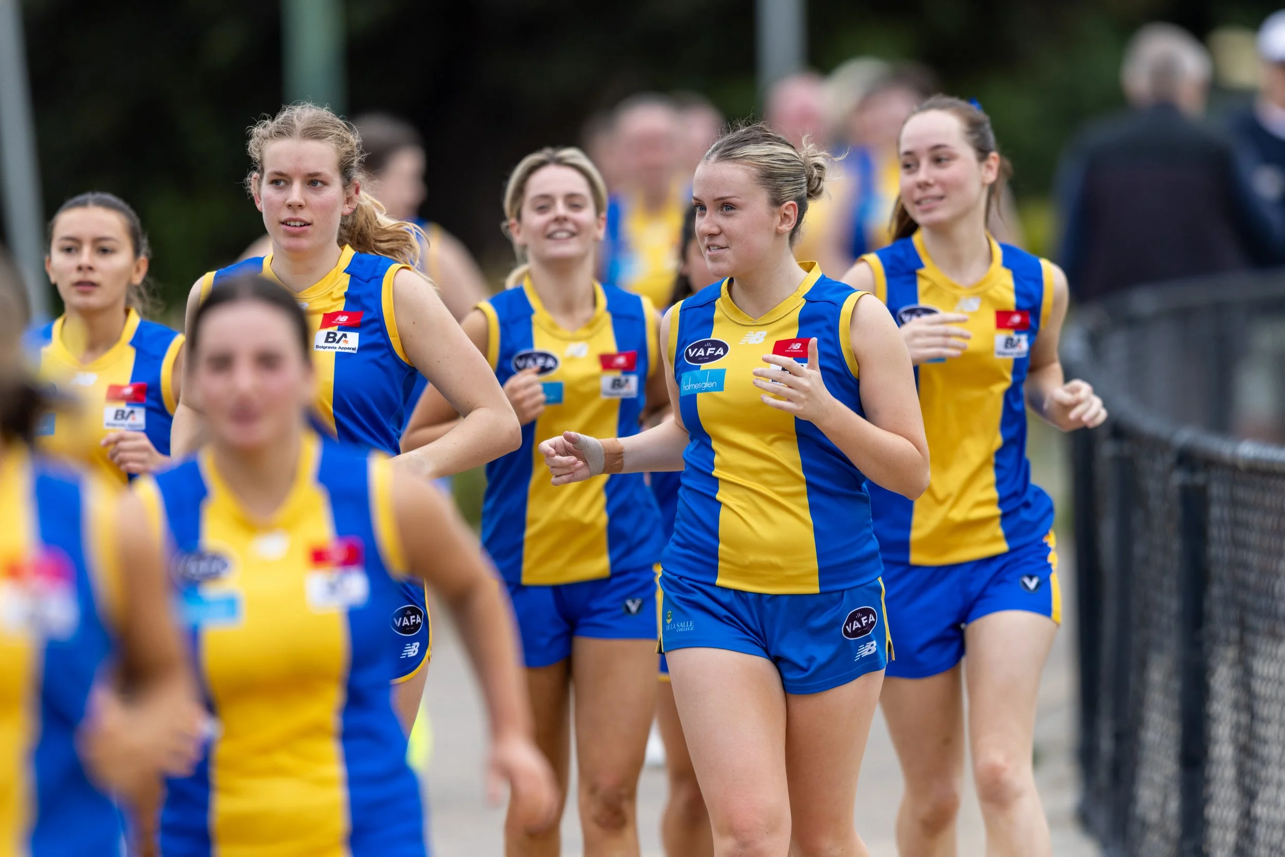 Group of young women De La Salle Footballers in blue and yellow athletic uniforms participating in a race.