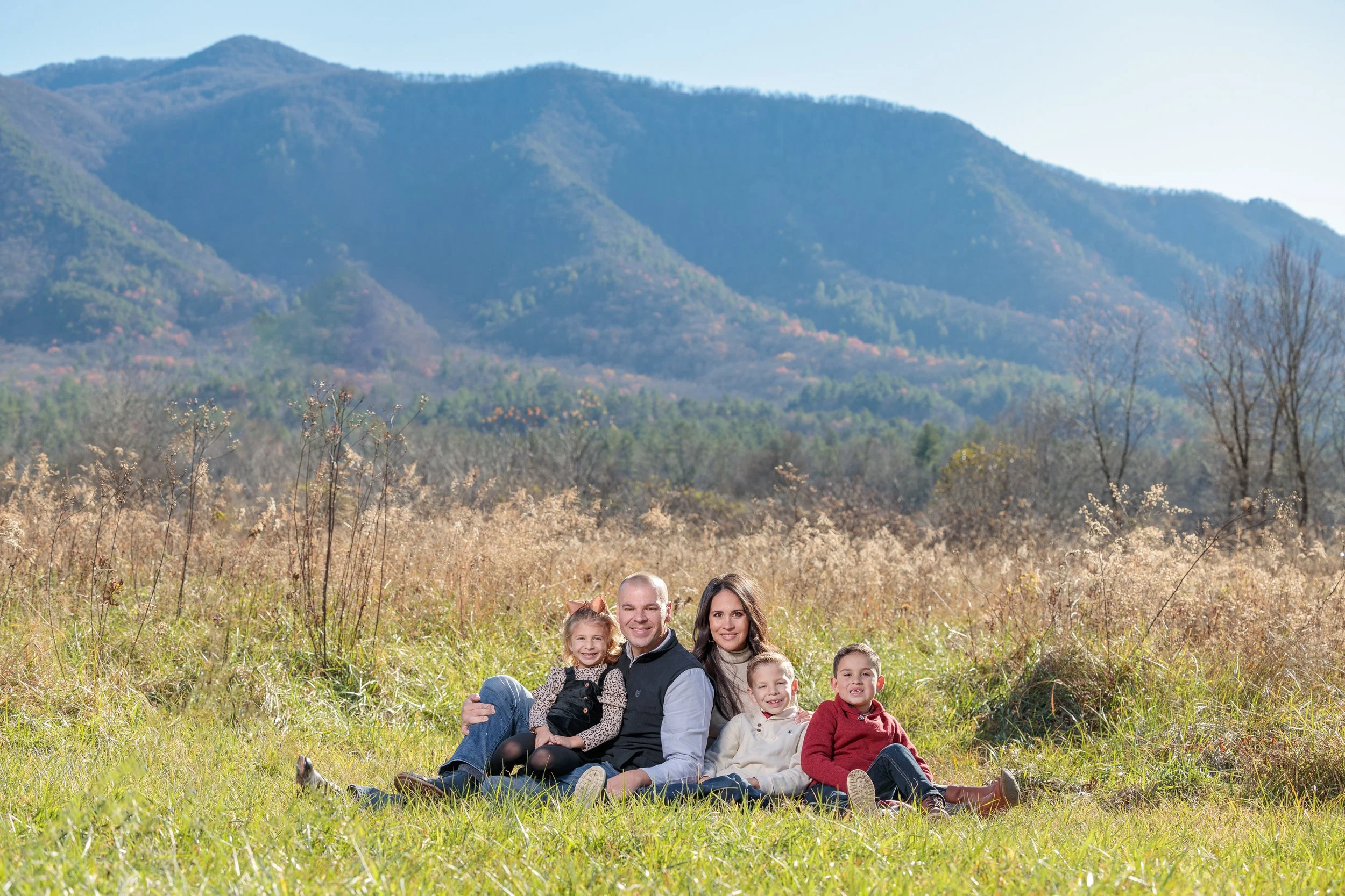 A young family poses before a beautiful mountain backdrop in Cades Cove in the Great Smoky Mountains National Park