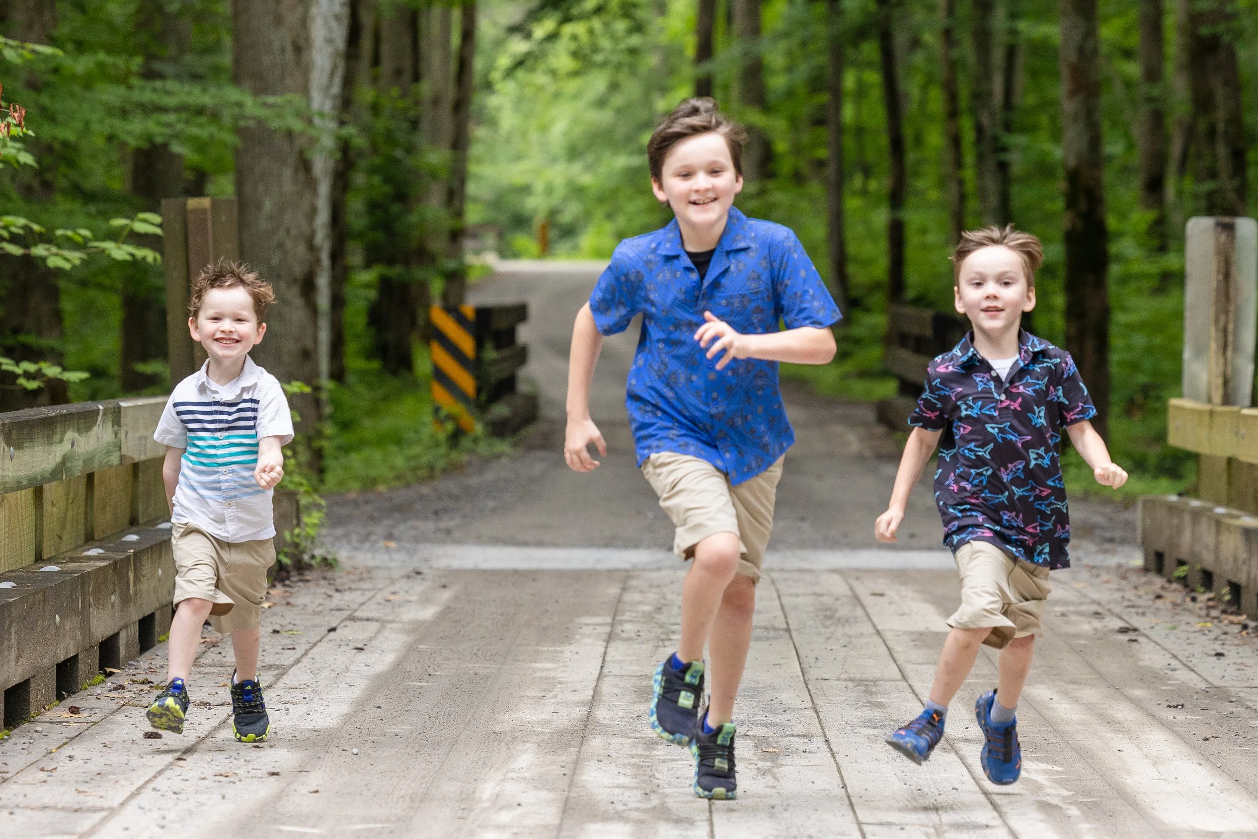 Three brothers laughing and running across a wooden bridge during their Smoky Mountain family photo session.