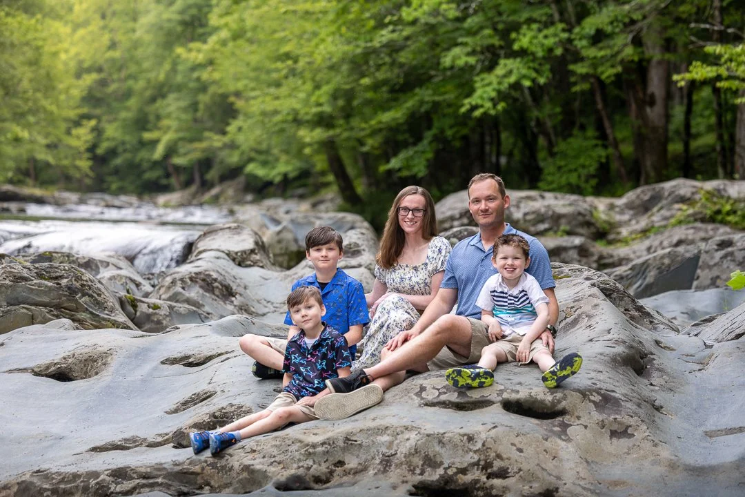 Family of five seated on smooth river rocks beside a mountain stream in Great Smoky Mountains National Park.