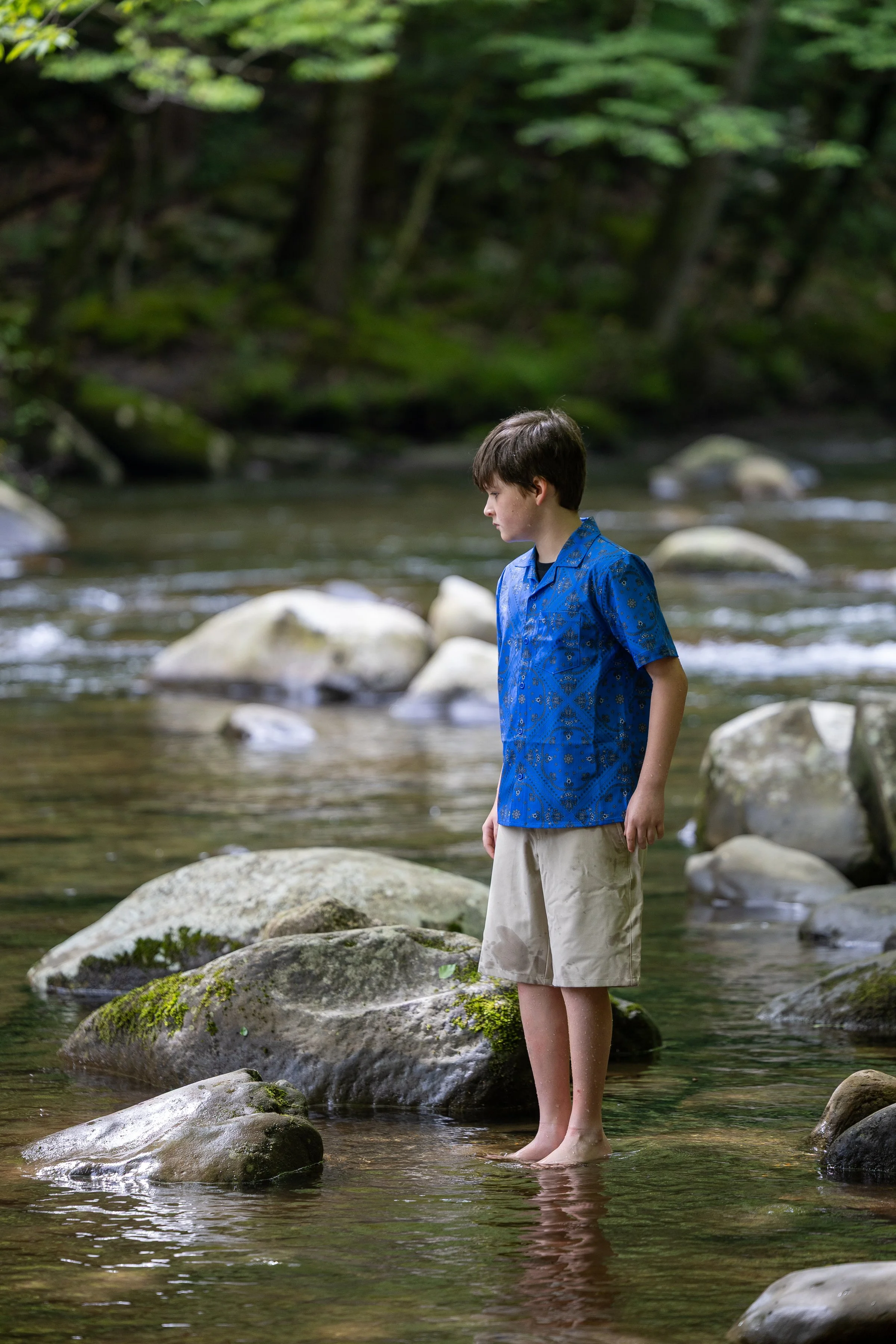 Boy standing barefoot in a shallow Smoky Mountain stream while exploring the water and rocks.