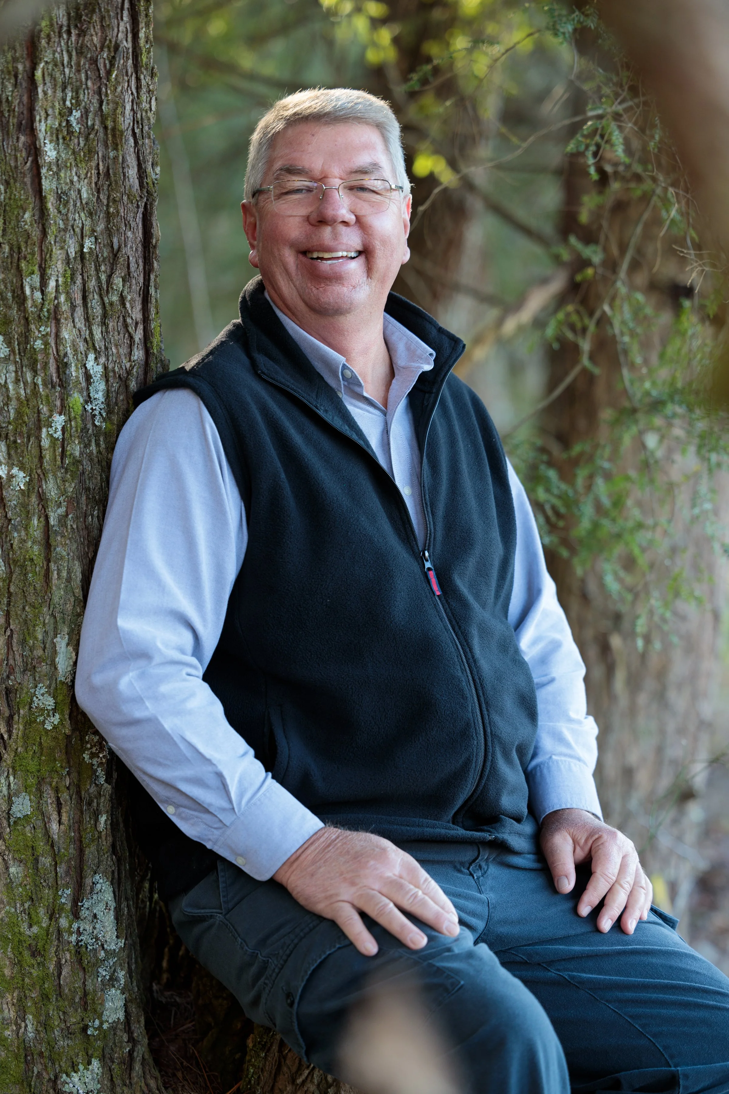 Portrait of a smiling grandfather beside a moss-covered tree in the wooded landscape of Cades Cove.