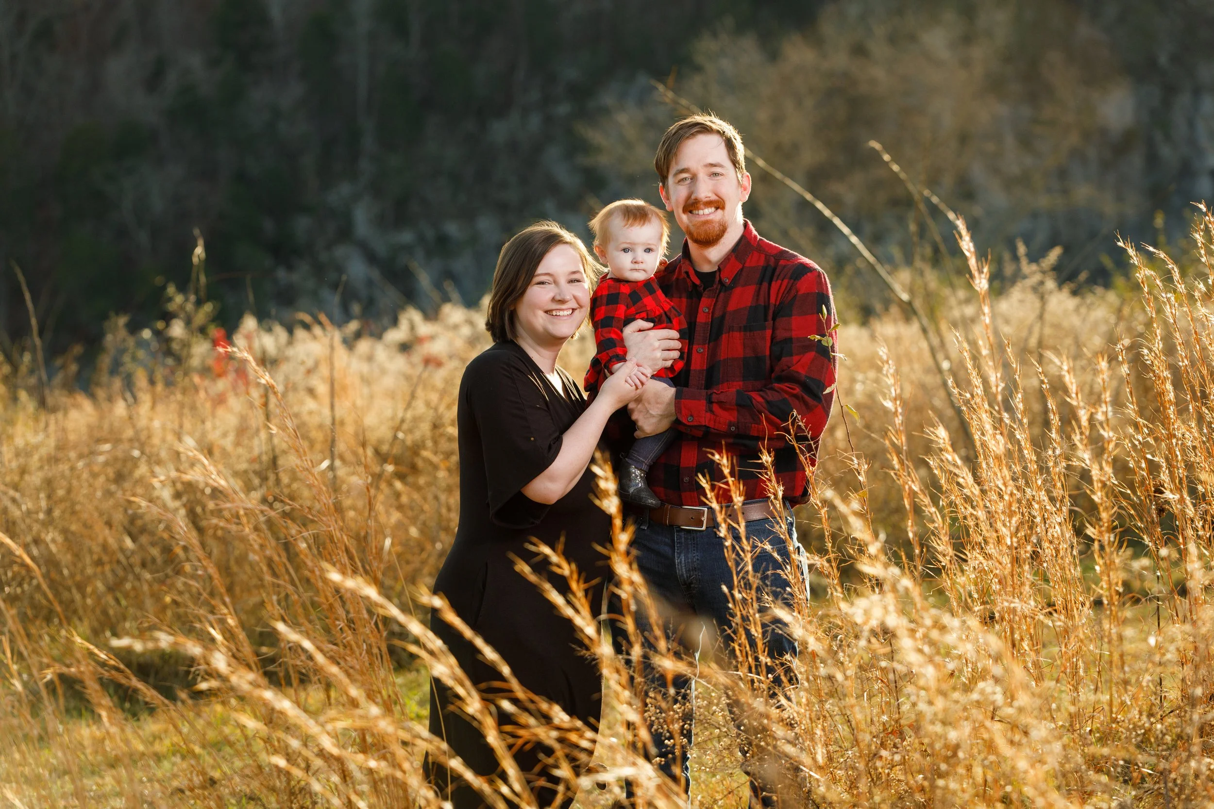 A couple with their baby girl are smiling in a warm Autumn setting in the Smoky Mountains