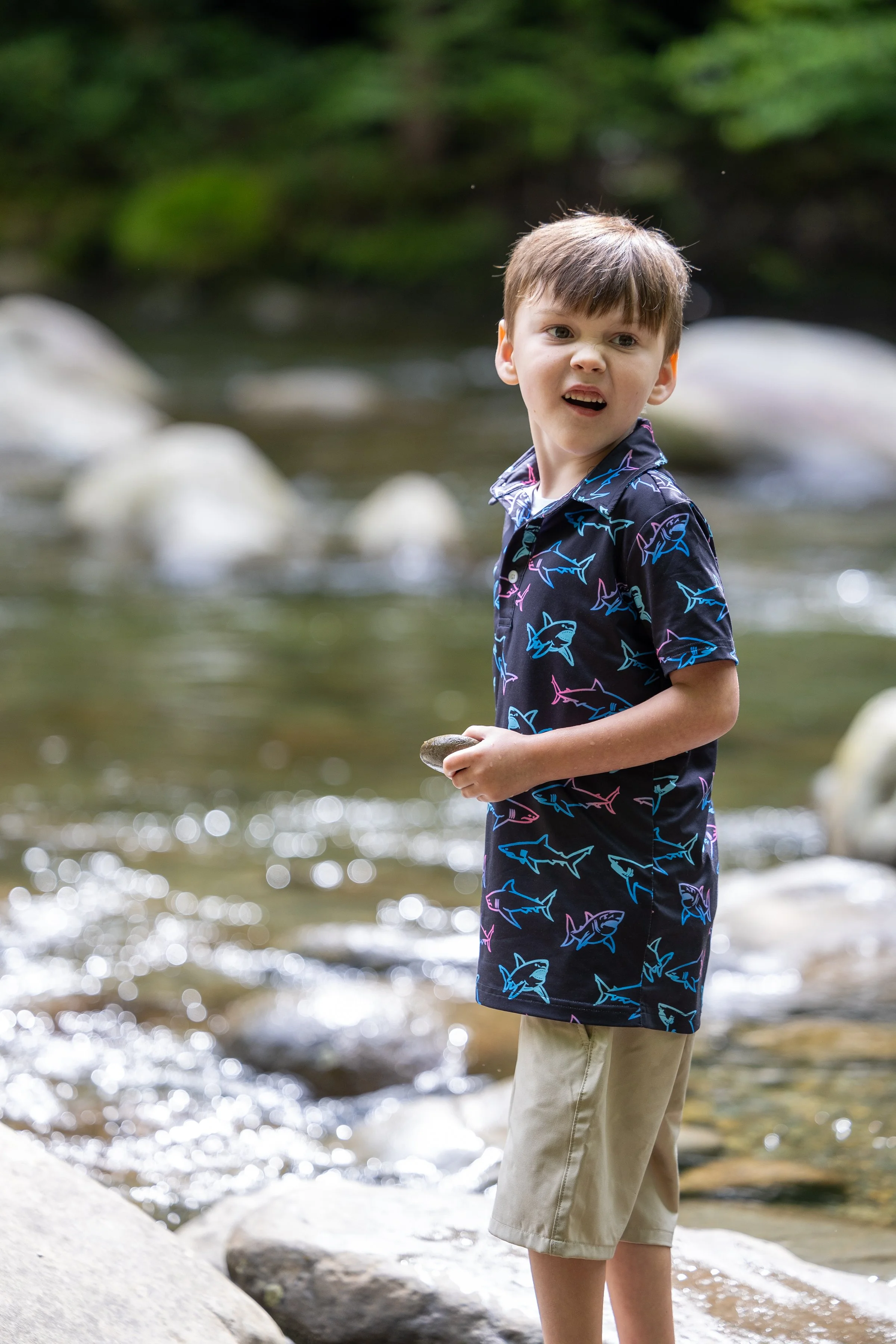 Young boy holding a river stone while playing beside a sunlit Smoky Mountain stream.