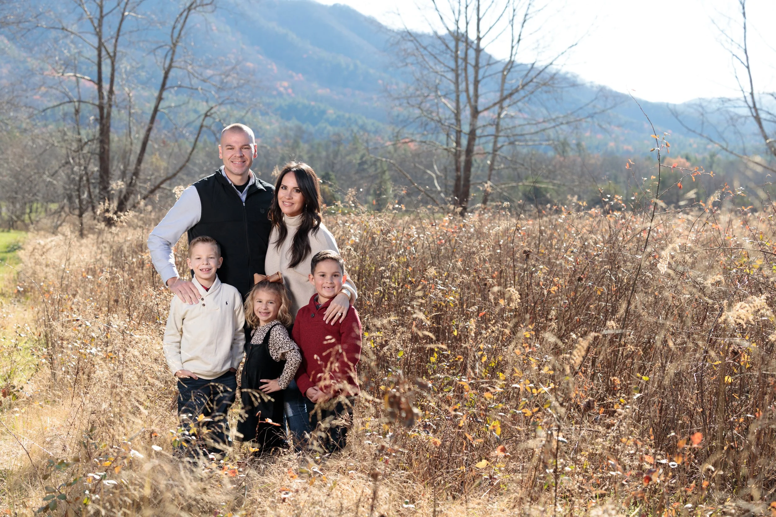 A family standing outdoors in a field in the Great Smoky Mountains, bathed by golden sun.