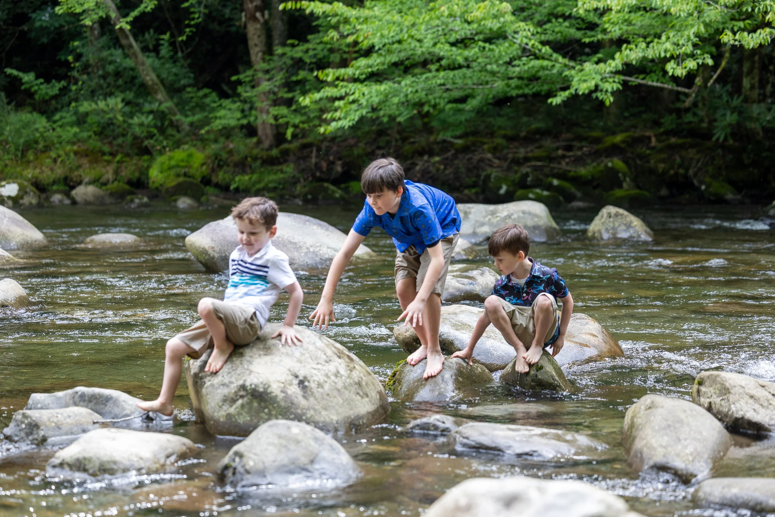 Three brothers climbing and playing on rocks in a shallow stream during a family photography session in the Smokies.