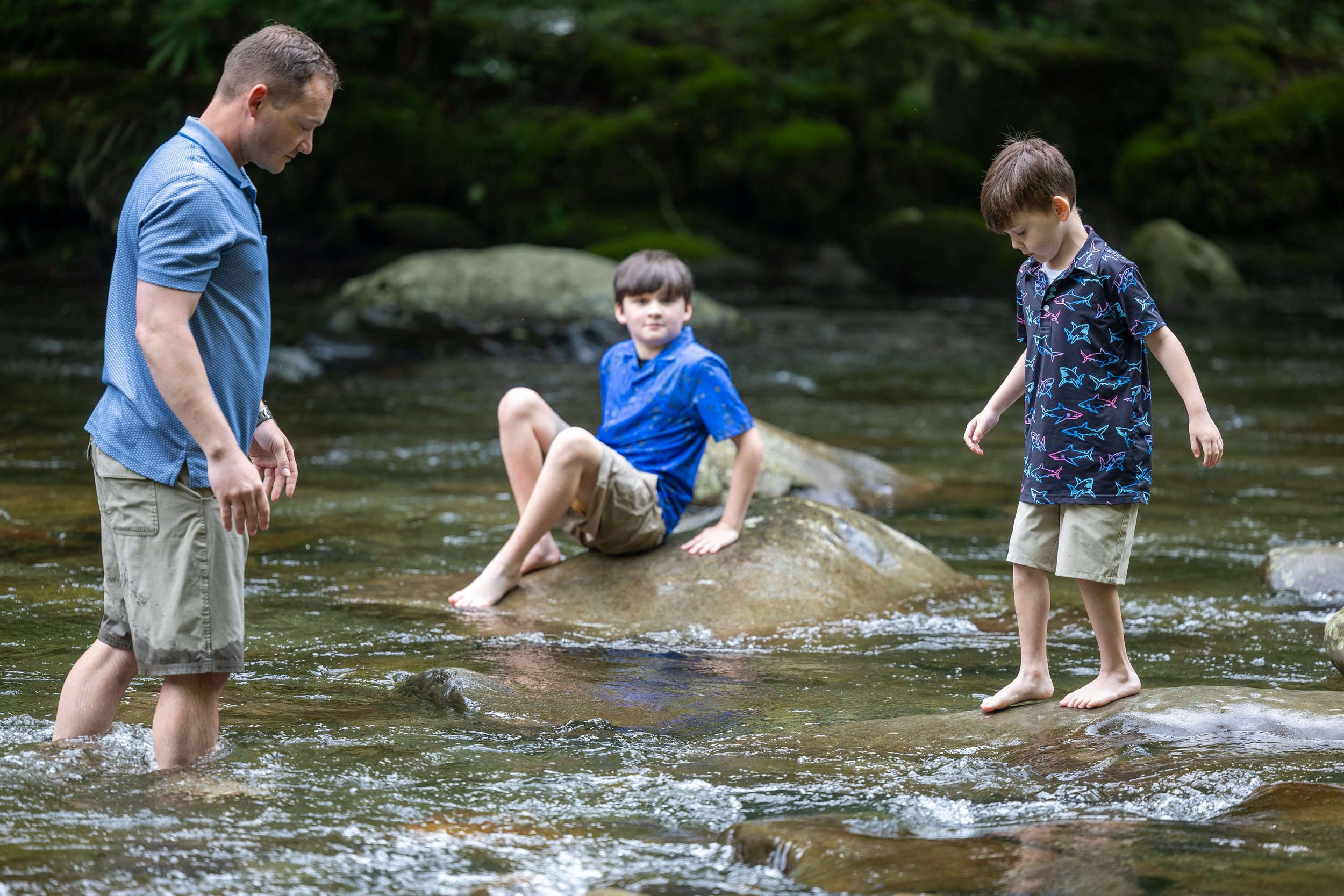 Father watching as his two sons play barefoot among the rocks in a shallow mountain stream.