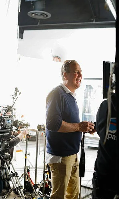 A man smiling and talking in a studio, with filming equipment and cameras around him.