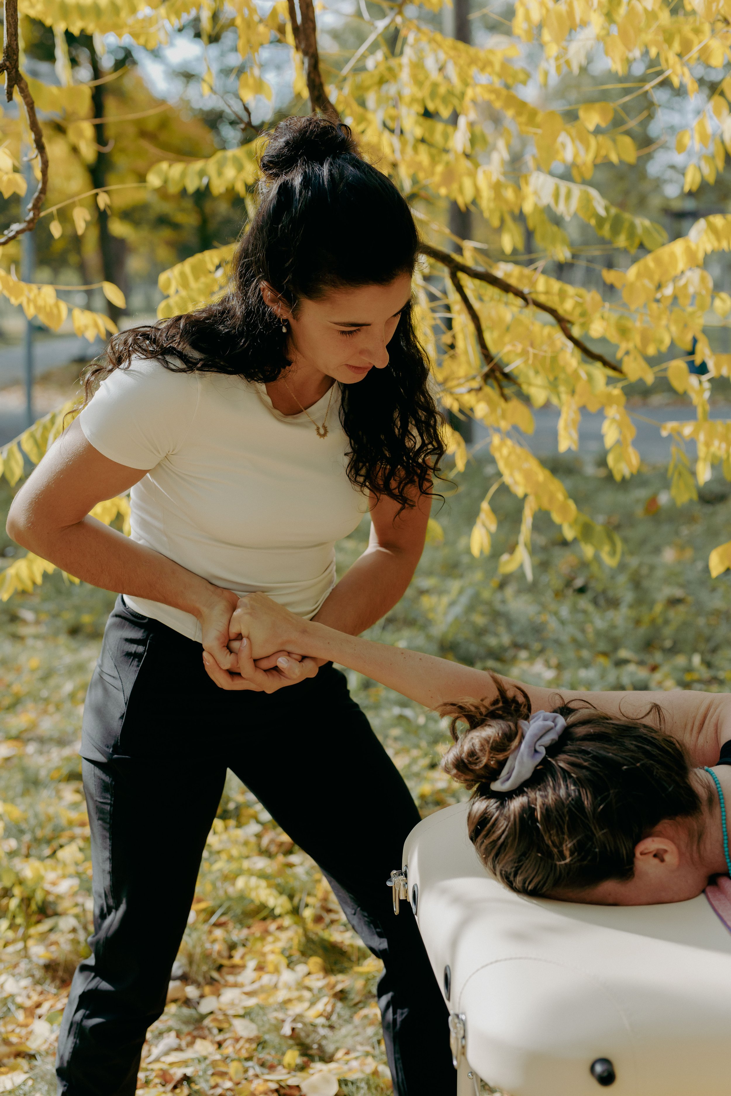 Eine Frau hilft einer anderen Person, die in einer Babybadewanne liegt, im Freien bei einem Spaziergang im Herbst. Es ist sonnig, und die Bäume haben gelbe Blätter.