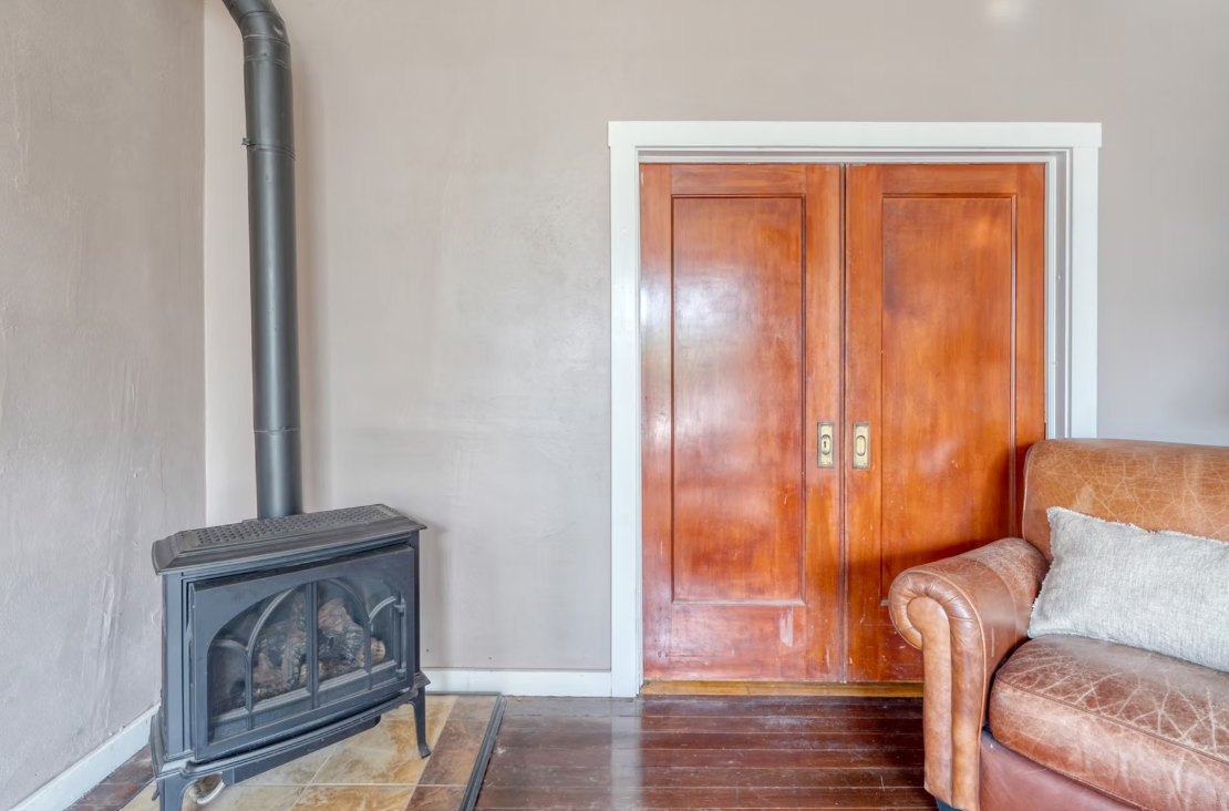 Living room corner with wood-burning stove, wooden sliding closet doors, and a leather armchair with a pillow.