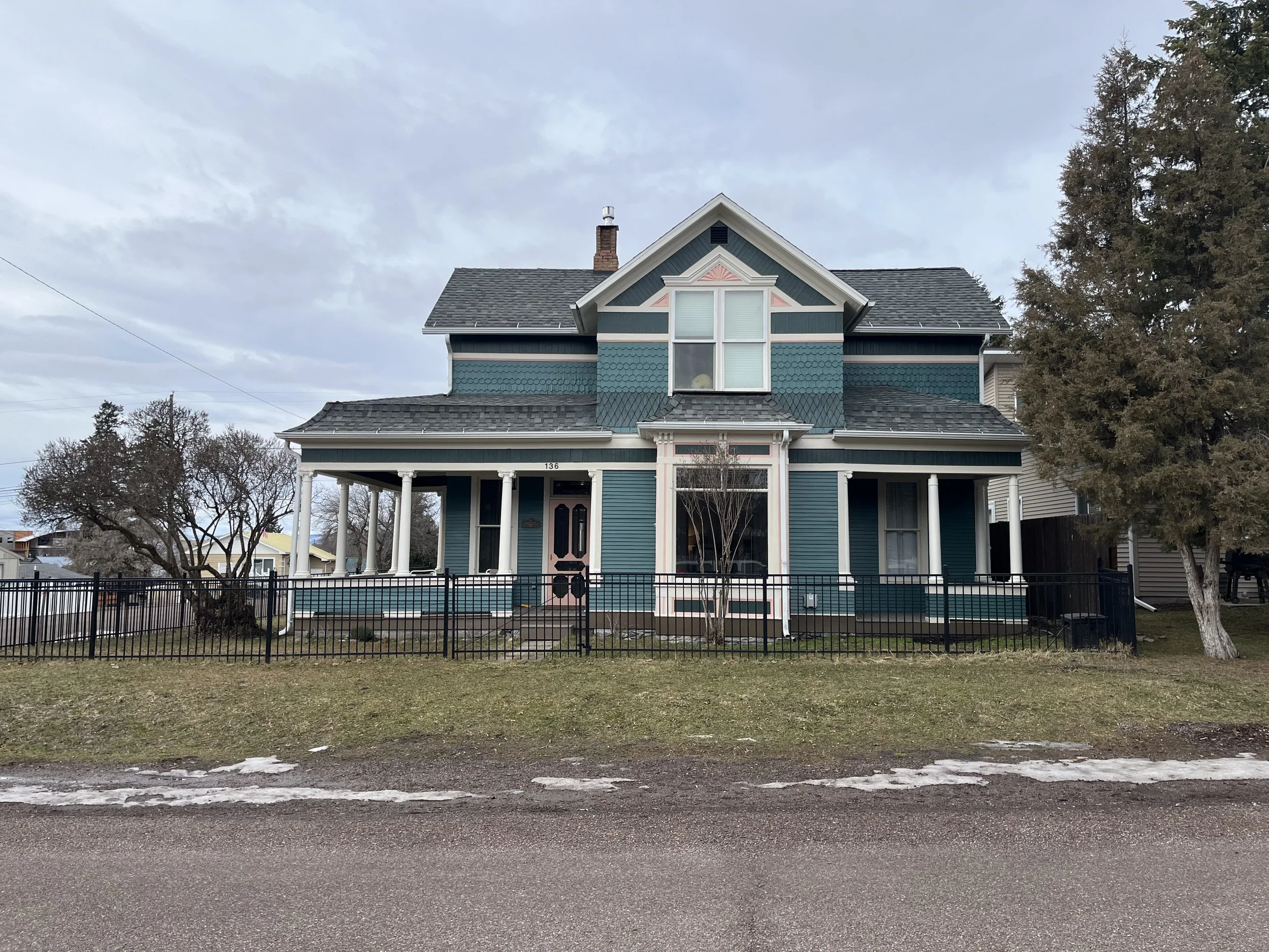 Photo of a blue two-story house with white trim, a front porch, and a small front yard, located in a neighborhood with bare trees and cloudy sky.