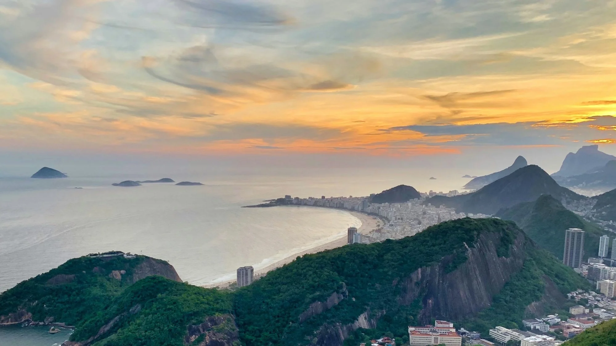 Copacabana Beach curving along the coast of Rio de Janeiro at sunset, seen from the green hills of Urca.