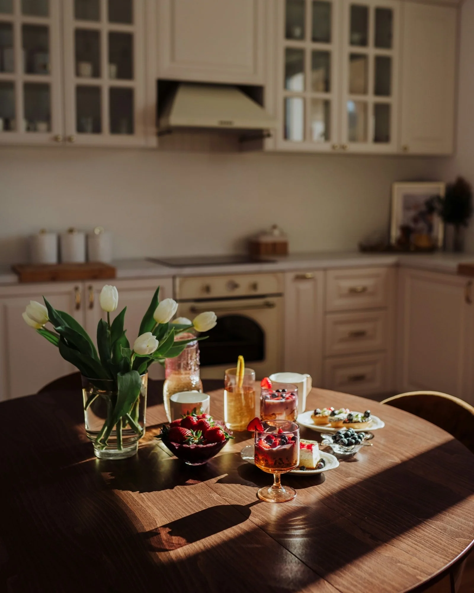 Early morning sun falls across a cream kitchen and a round wooden table with white tulips.