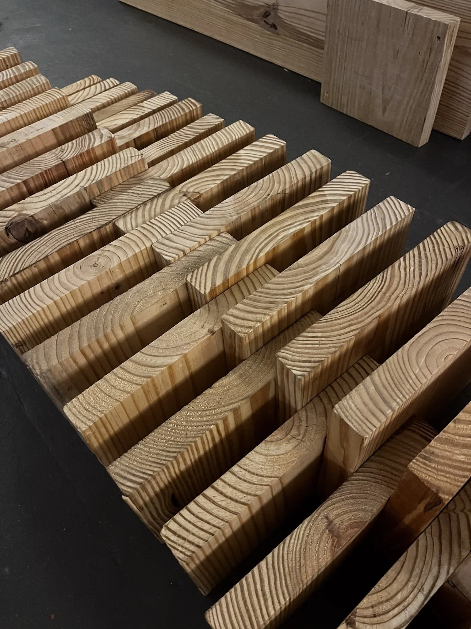Stacked wooden planks and pieces of lumber placed on a dark surface.